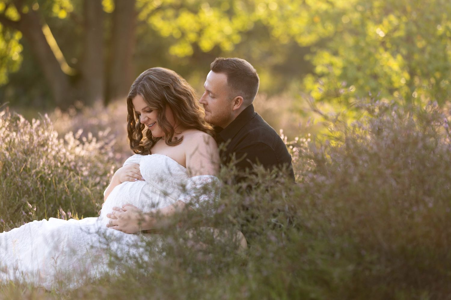 A couple shares a tender embrace outdoors during golden hour with soft sunlit trees in the background.
