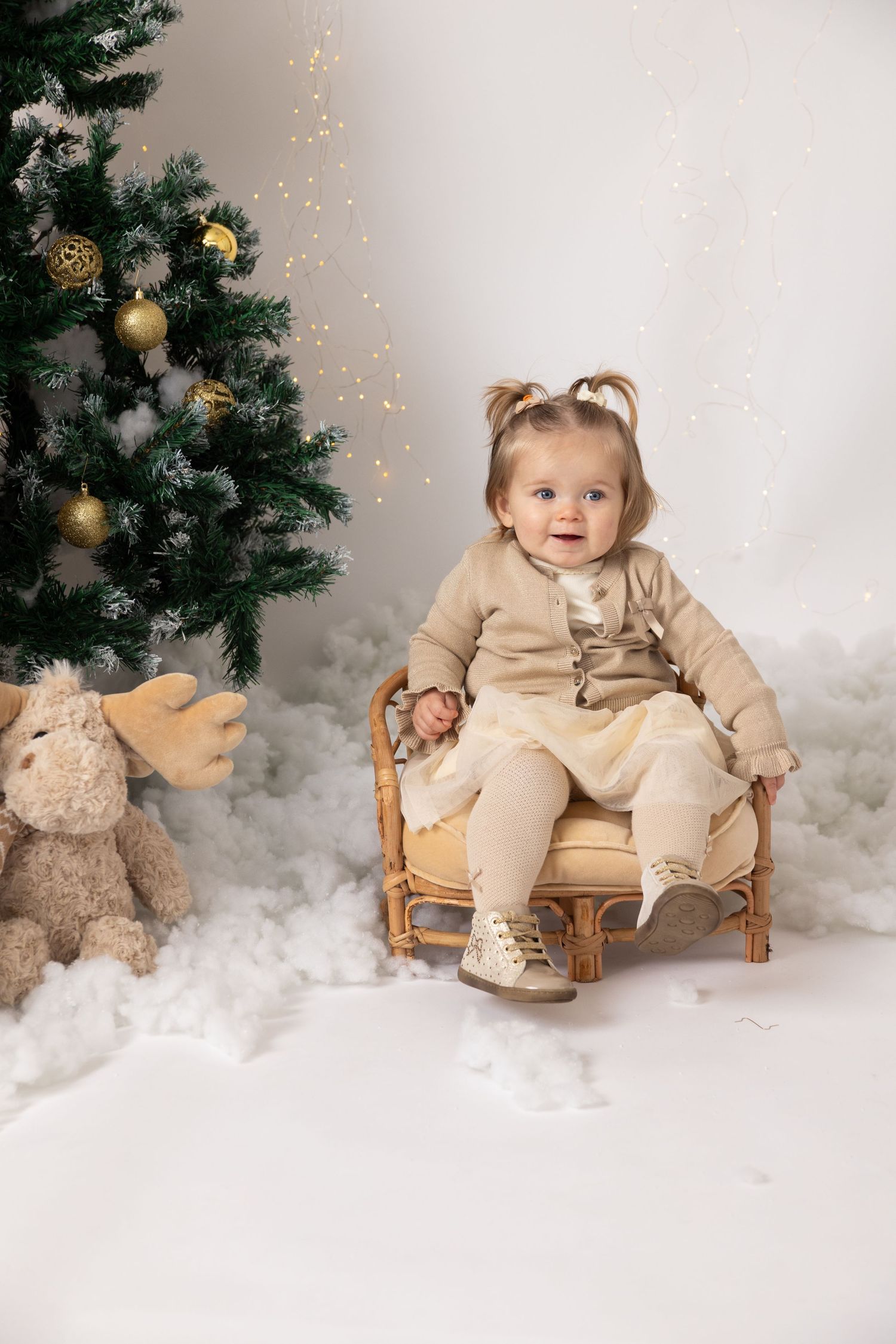 A cozy winter studio setup with soft white clouds, Christmas trees, and gold ornaments in a dreamy beige aesthetic.