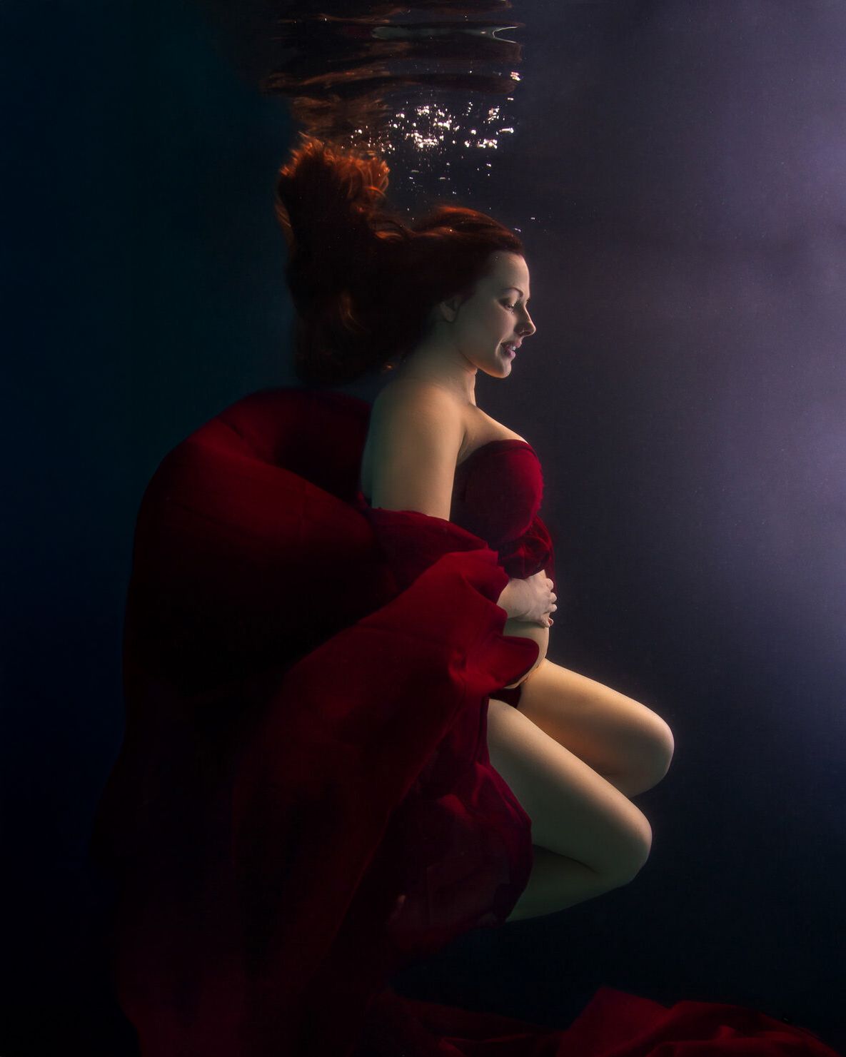 A figure in a red dress emerges from darkness in a dramatic low-key portrait series.