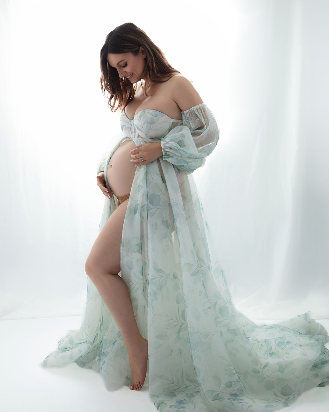 Maternity photo session featuring an ethereal mint green flowing dress against a light backdrop.