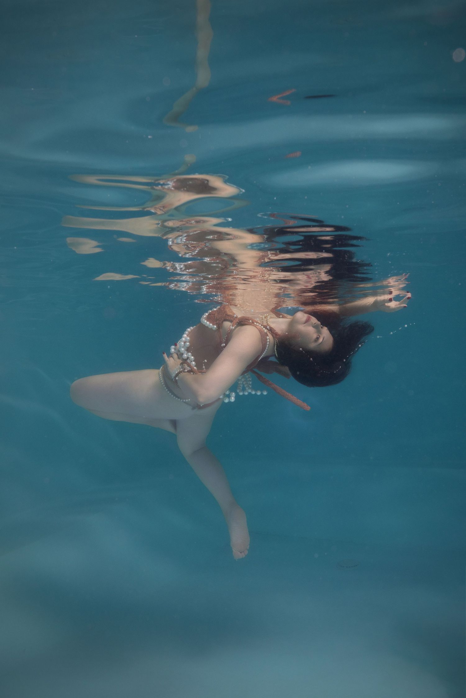 Woman in white bikini poses gracefully underwater in a clear blue pool, hair flowing, captured in an artistic underwater photograph.