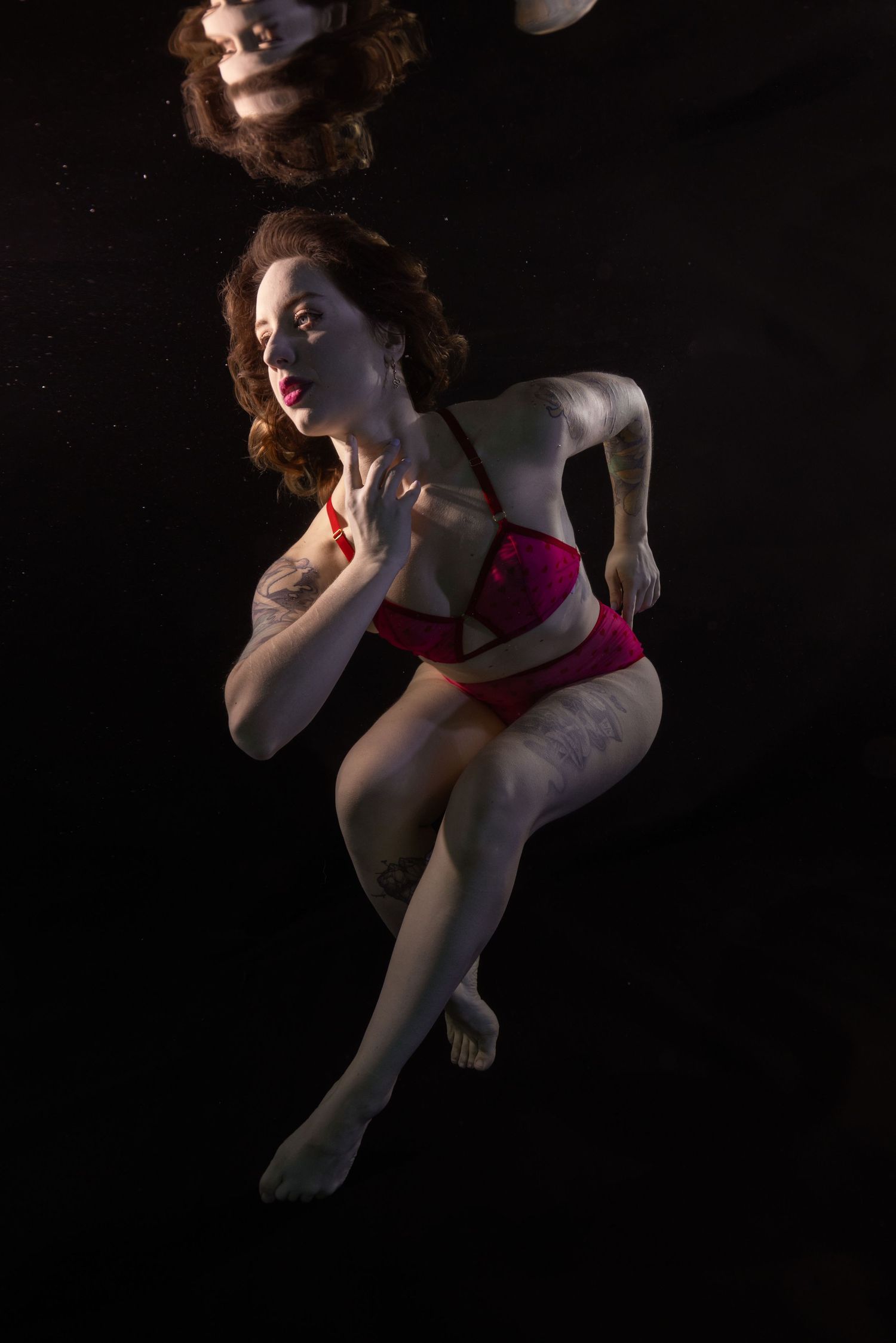 Woman in red lingerie poses gracefully underwater against a dark background.