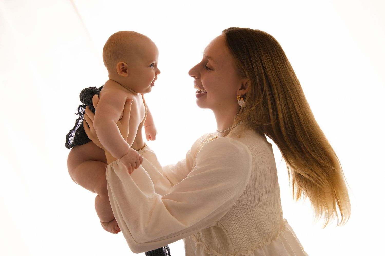 A joyful moment captured in soft lighting as a parent lifts up a smiling baby wearing dark clothing.