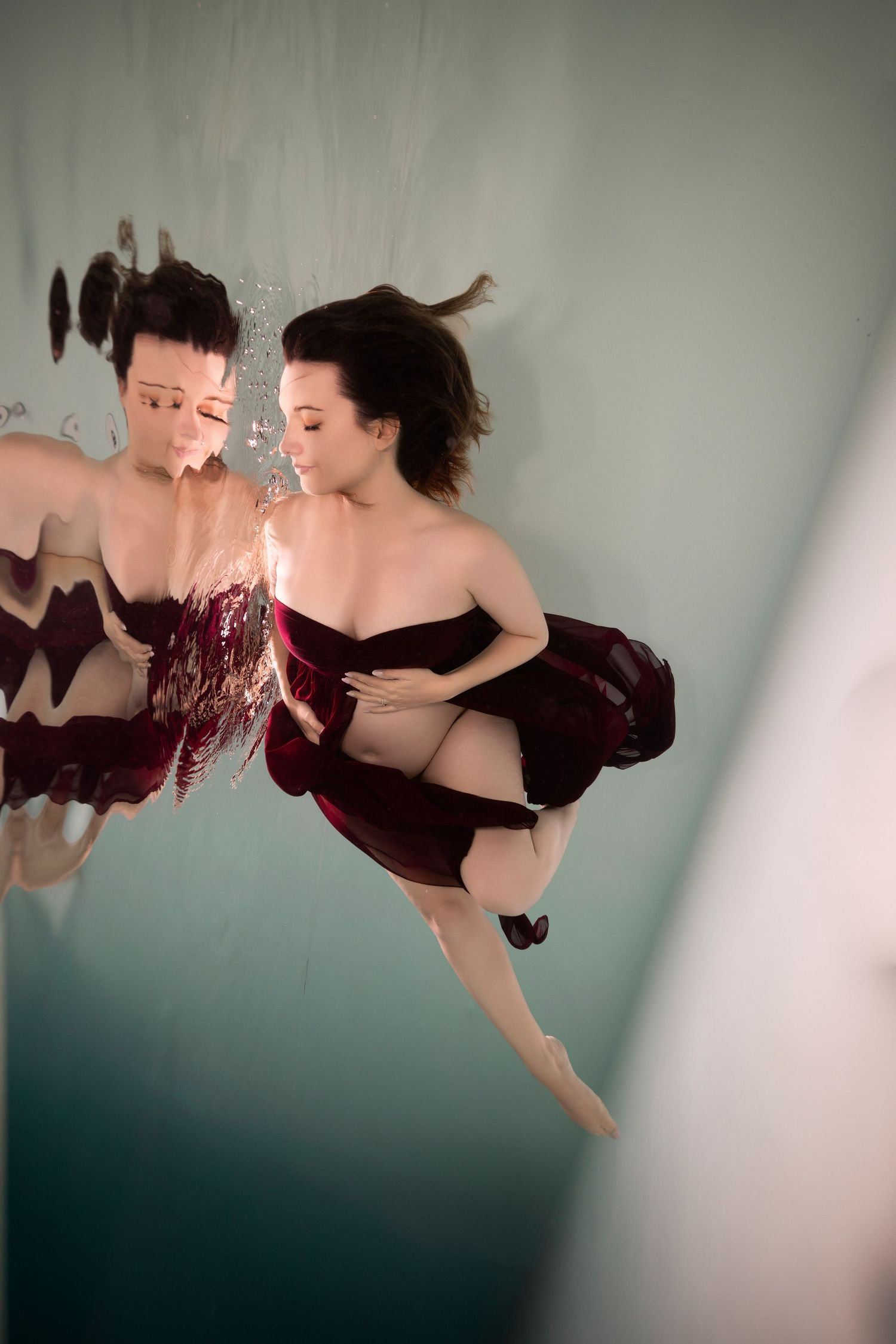 Underwater dancer in burgundy dress floats gracefully through dark aquatic space in artistic photo sequence.