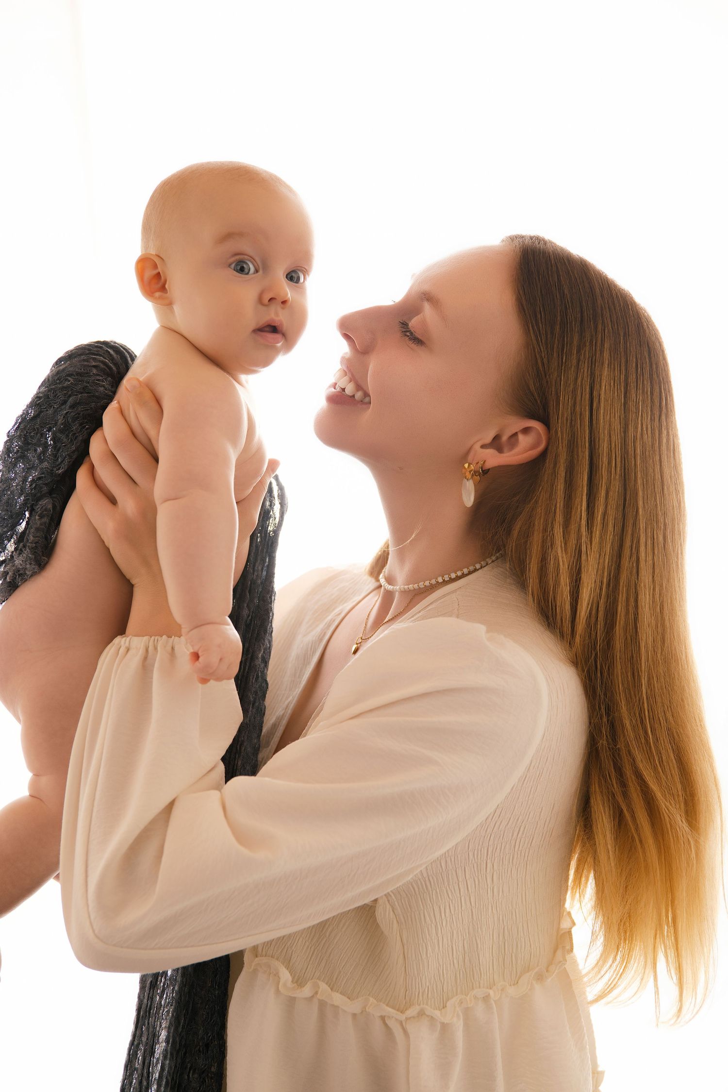 A sequence of photos showing a parent in white lifting a baby in multiple poses against a light background.