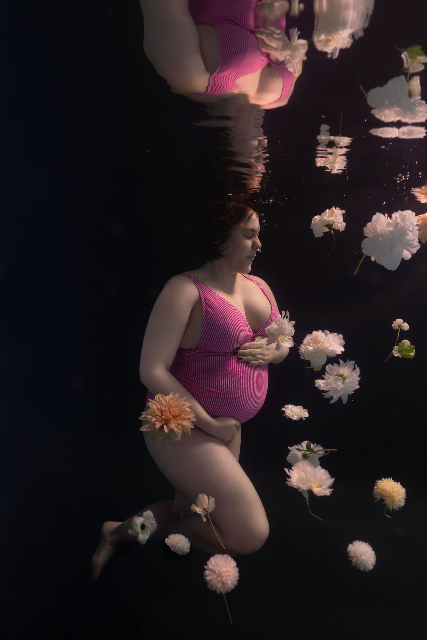 A maternity photoshoot with white and peach flowers floating against a dark background.