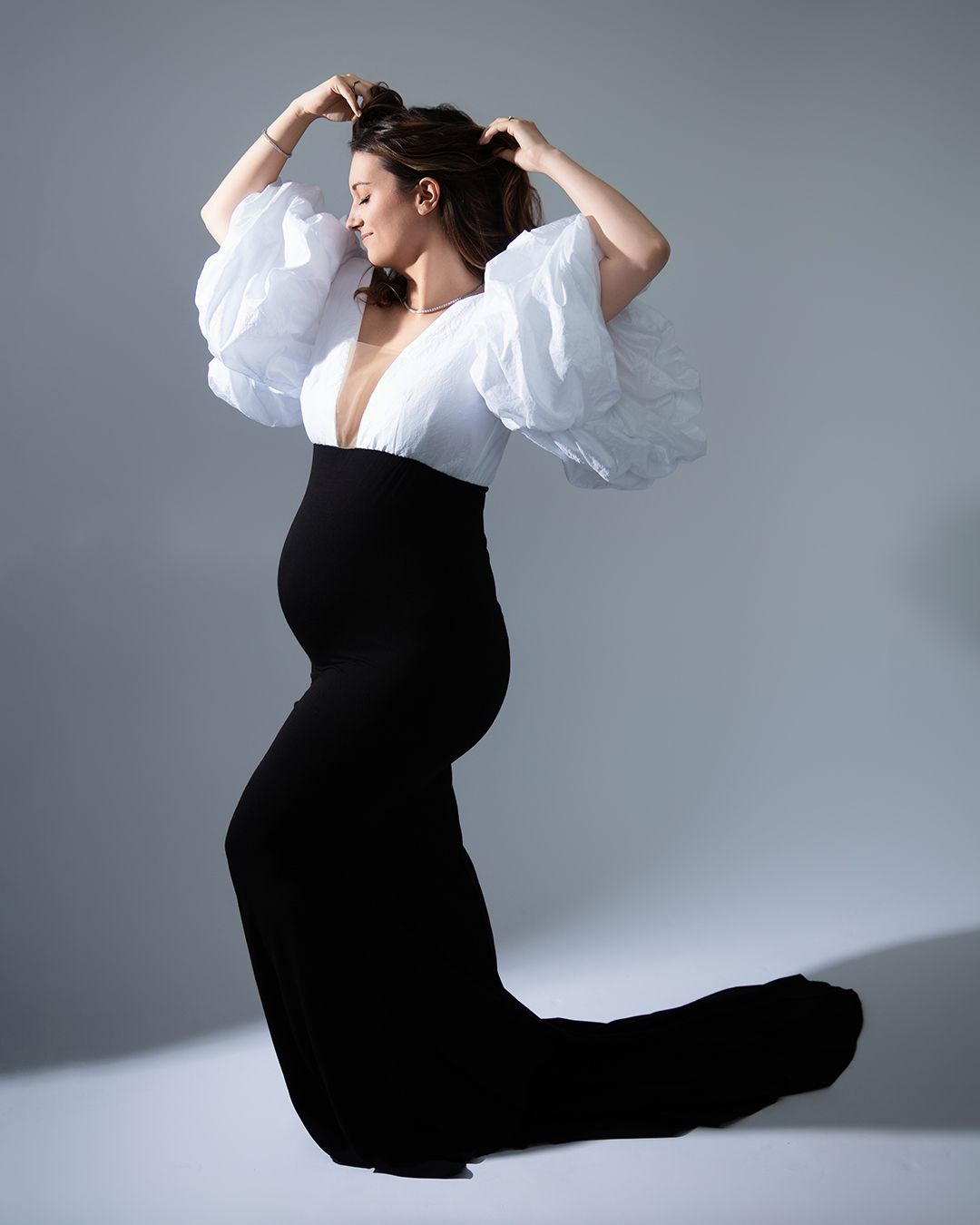 A dancer in a black dress and white top performs a graceful split pose against a light gray backdrop.