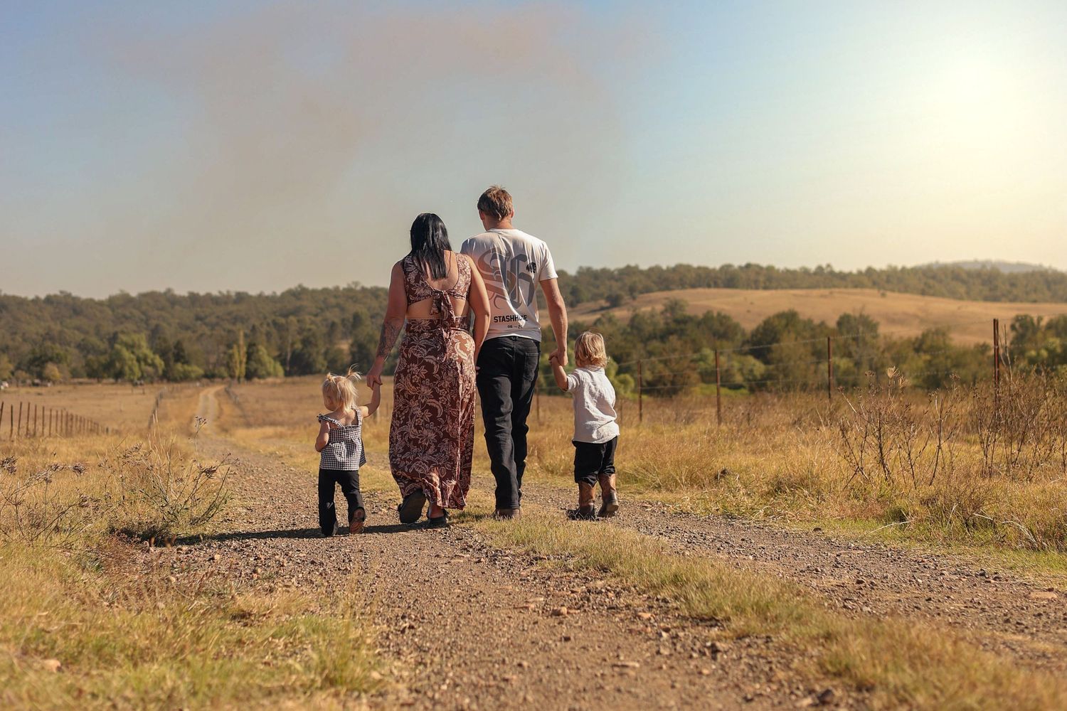 Family of four walking down a rural dirt path with rolling fields and trees in the background.