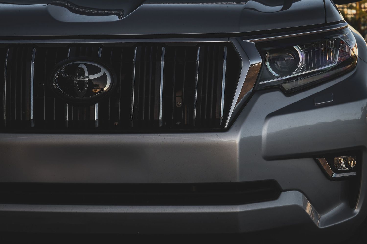 Close-up view of modern Toyota vehicle front grille showing headlight detail and brand emblem in dark lighting conditions.