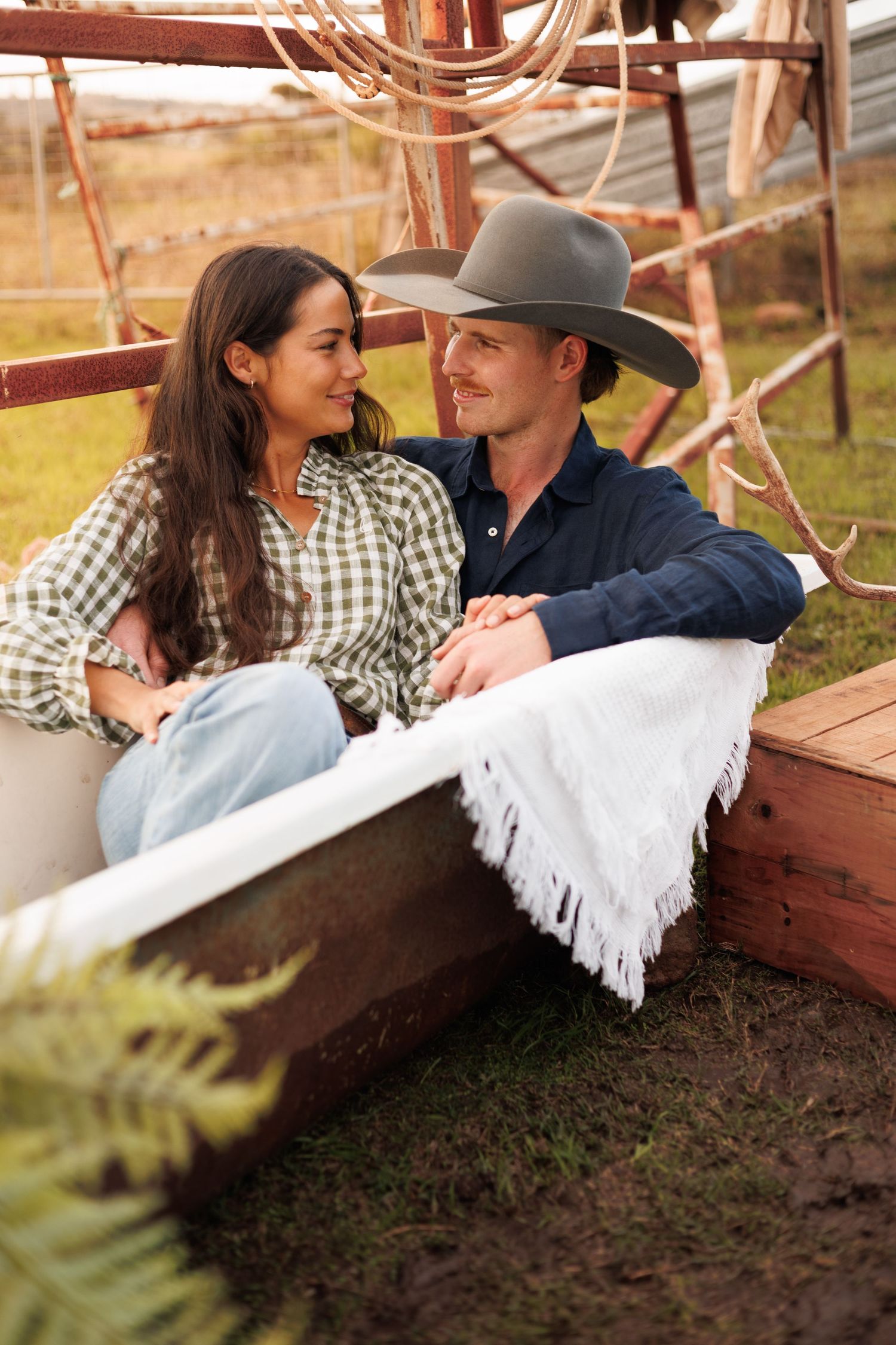 A couple in plaid shirts and cowboy hat sitting together in a rustic outdoor setting on a farm.