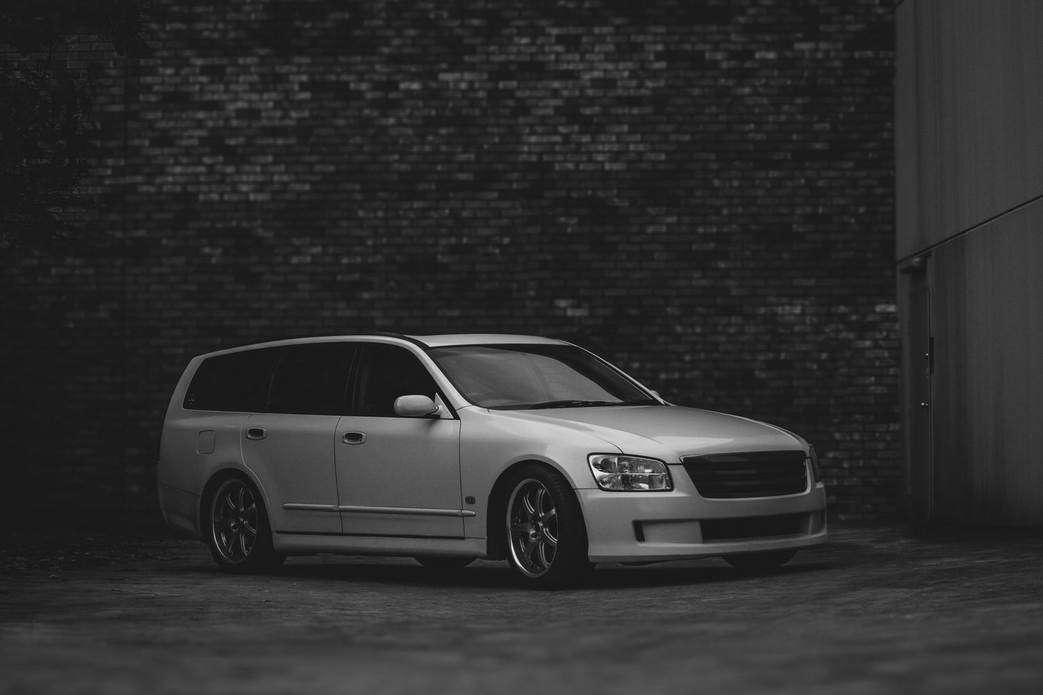 A lowered station wagon parked against a dark brick wall.