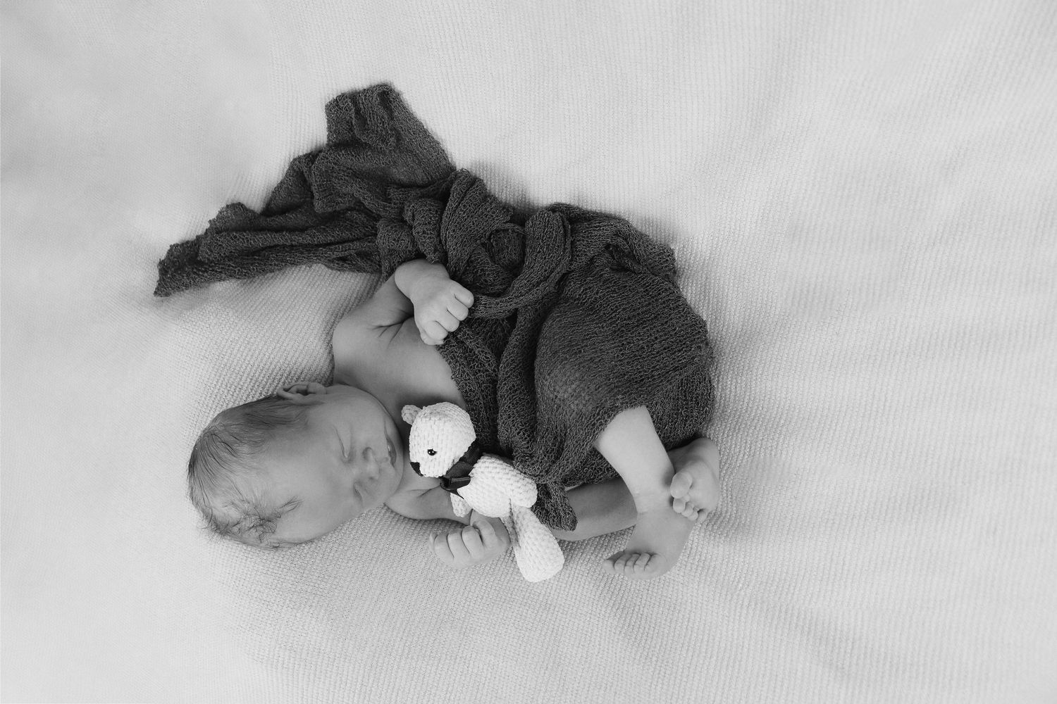 A baby sleeping peacefully in dark clothing while cuddling a small stuffed animal.