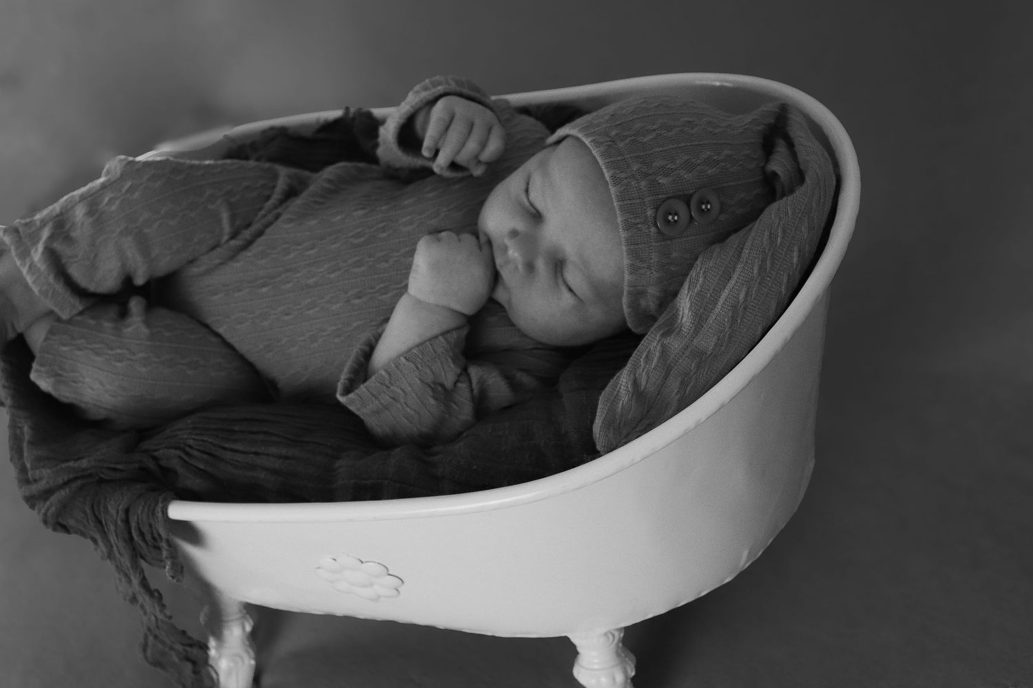 Sleeping newborn baby curled up in a cushioned white bath, captured in black and white.