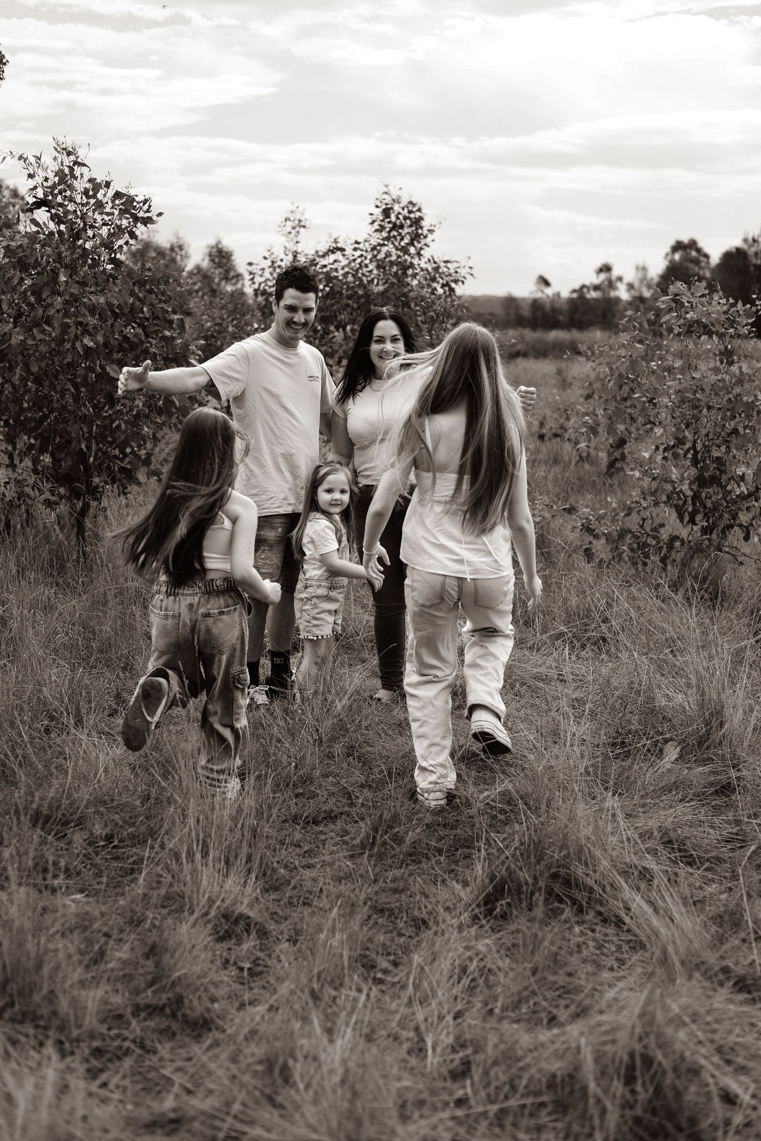 Black and white photo of a happy family with three children walking together through a lush green field.