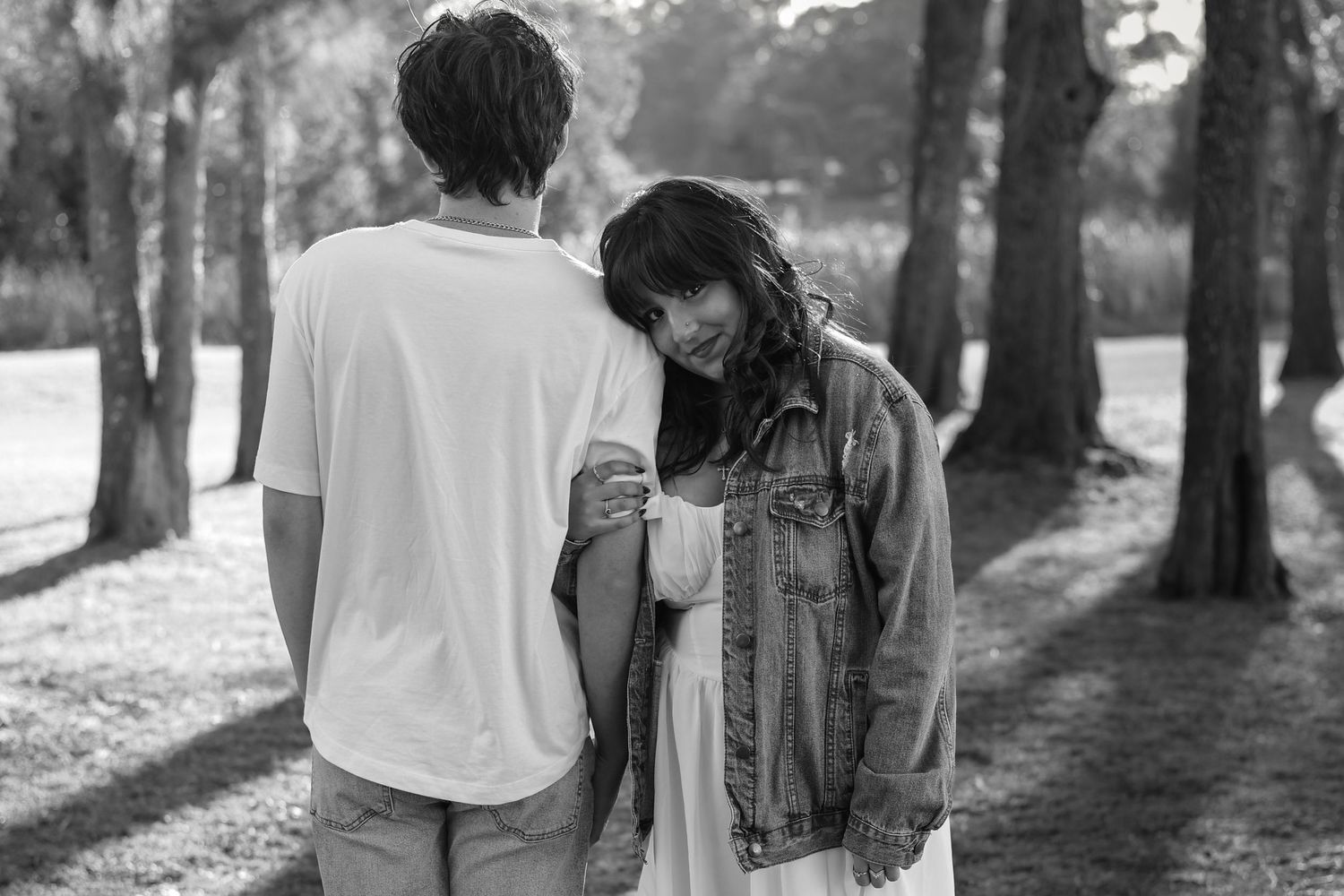 Black and white photo of a couple sharing a tender moment among trees in a sunlit park.