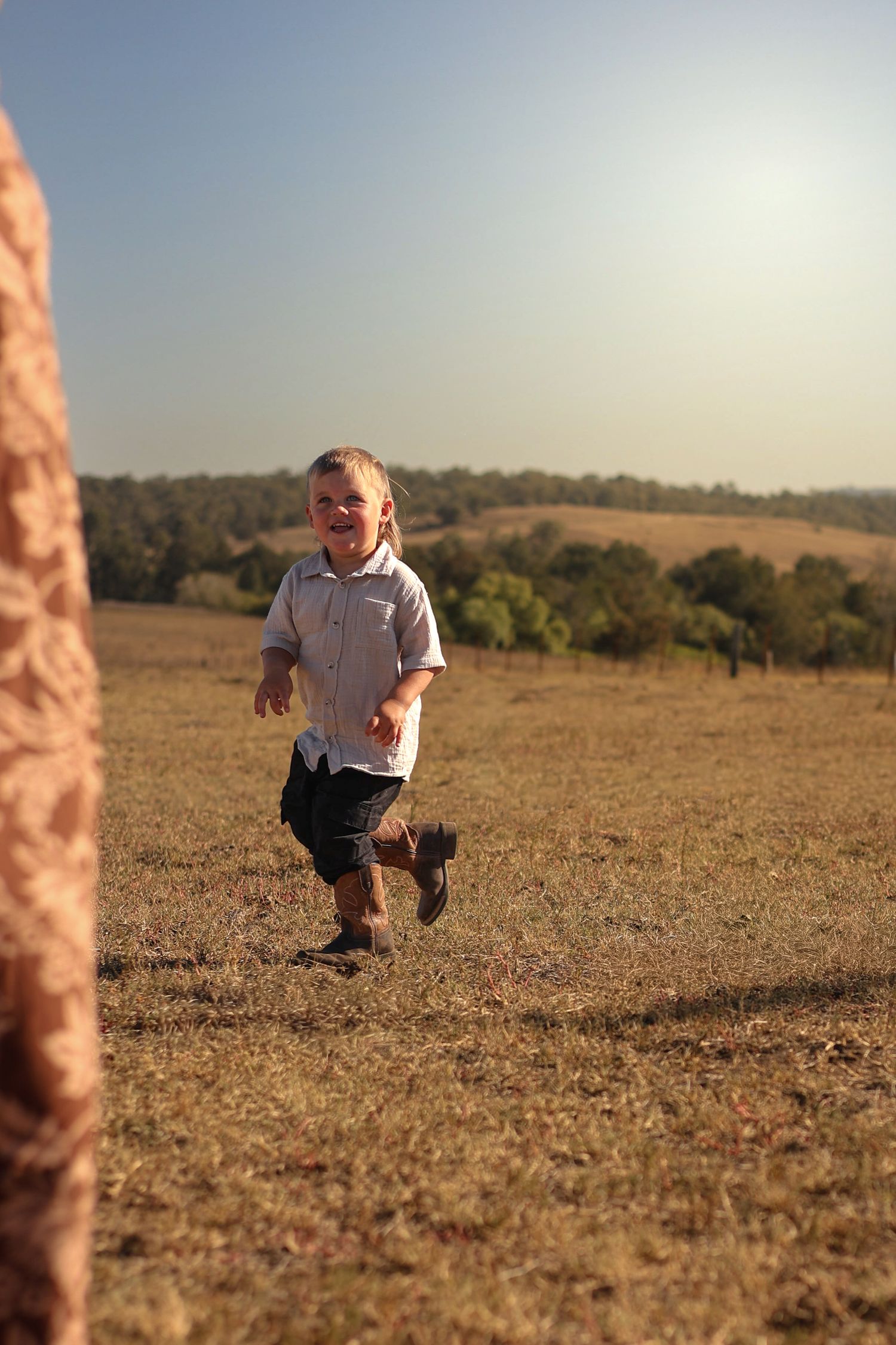 A happy toddler boy runs through a sunny open field toward the camera, smiling joyfully on a clear day.