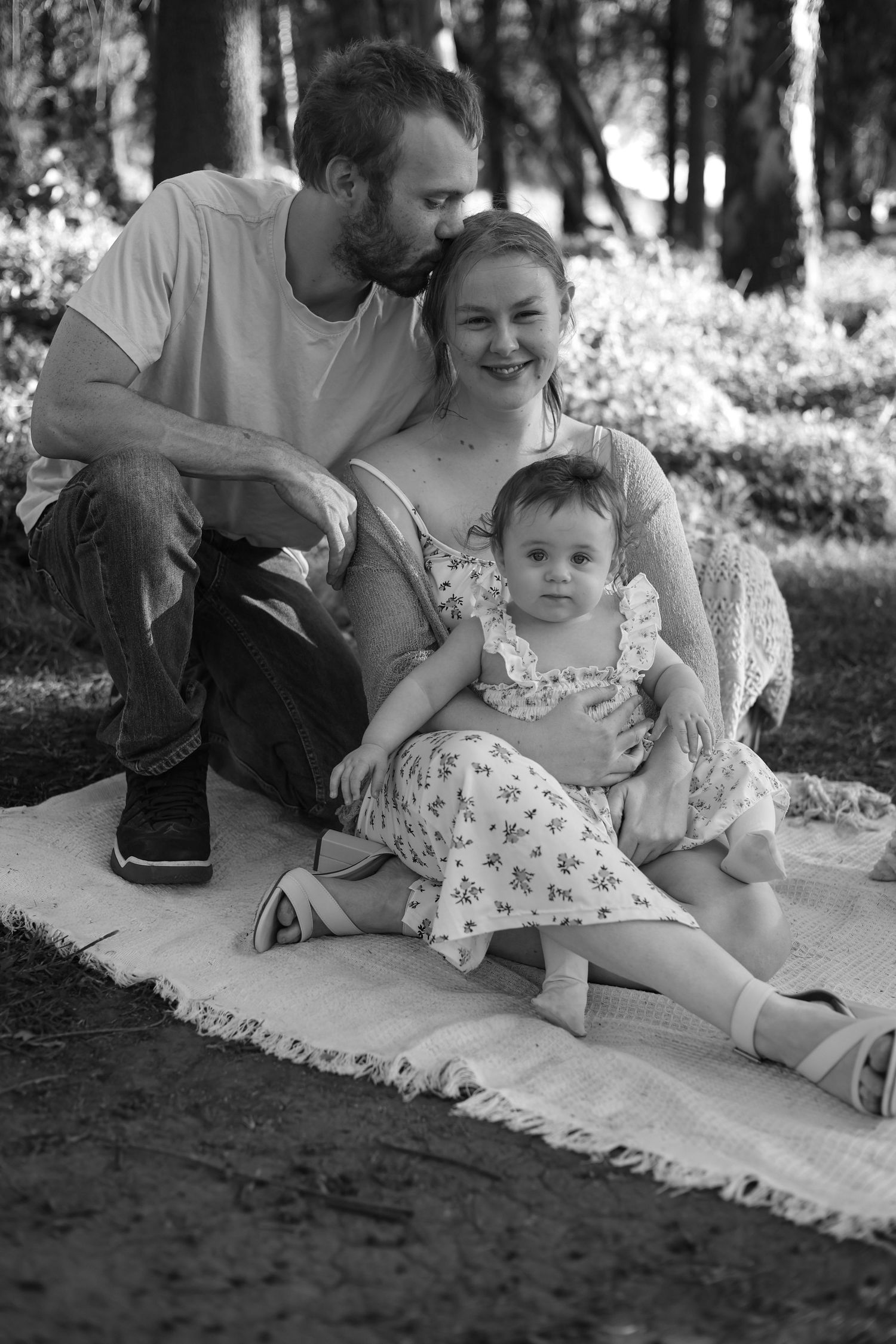 Happy family with baby girl sitting on blanket in park, black and white photo.