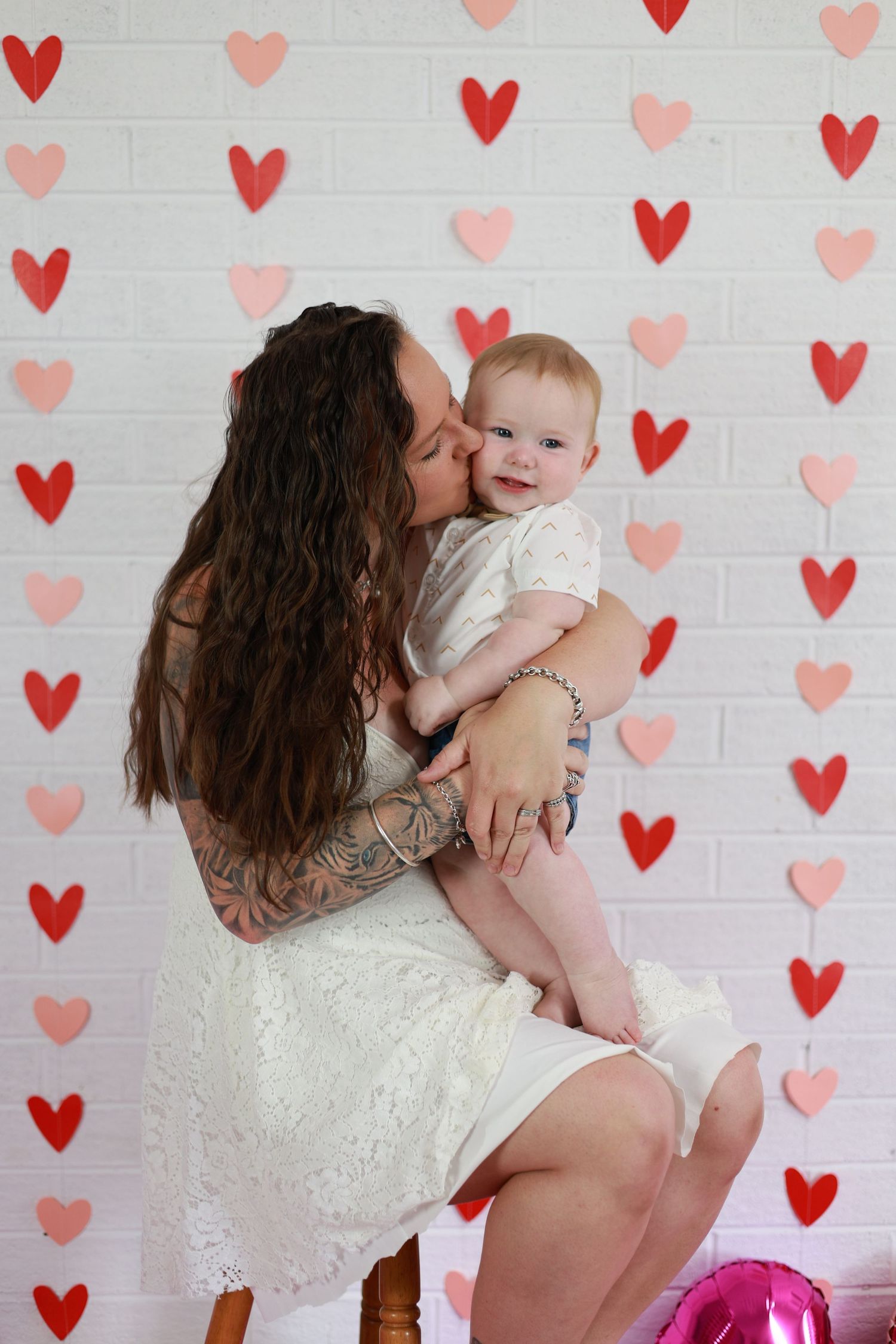 A loving moment captured against a wall decorated with pink and red paper hearts for Valentine's Day.