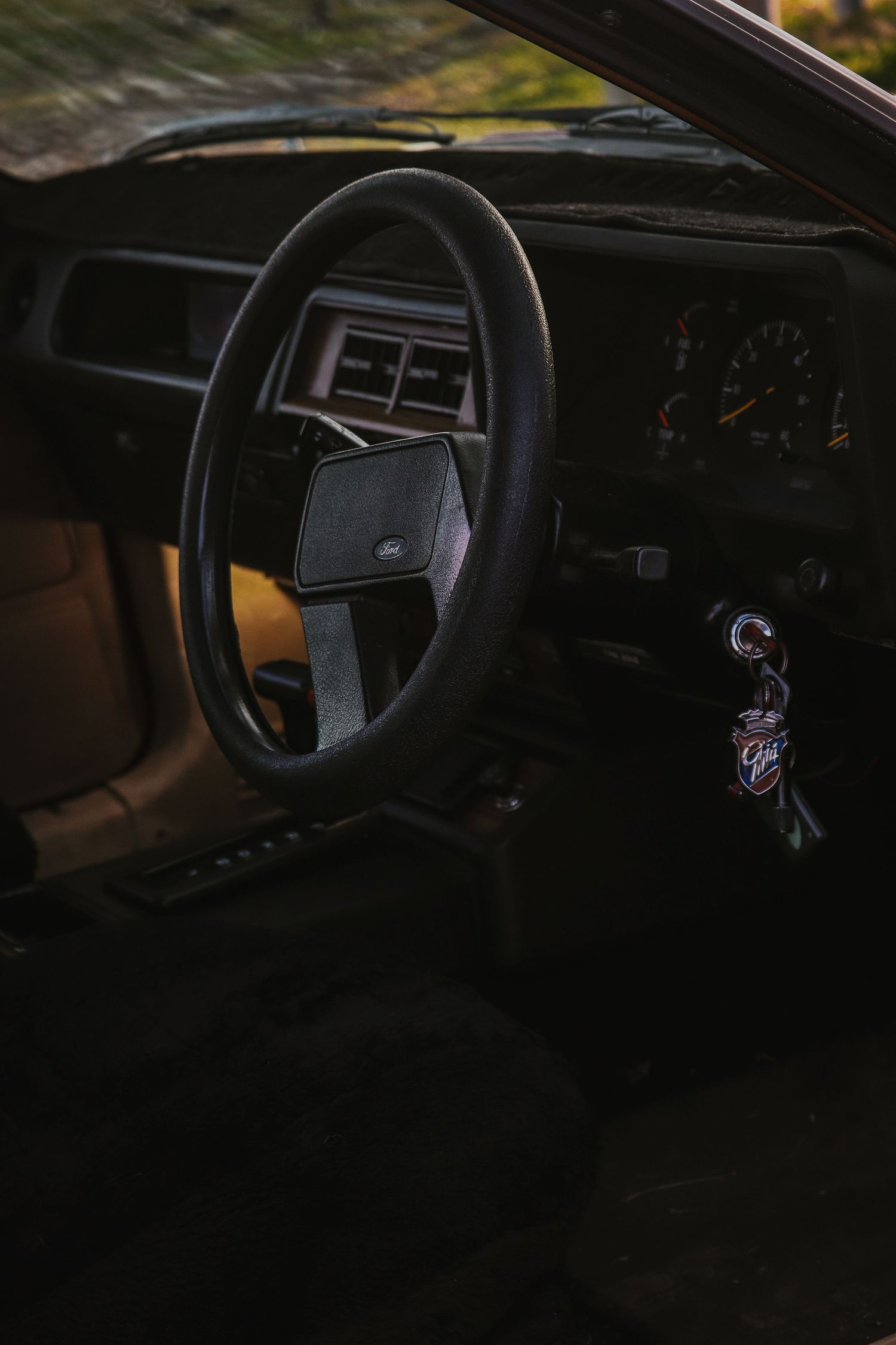 Dark interior of a car showing black steering wheel and dashboard with keychain hanging from ignition at dusk.