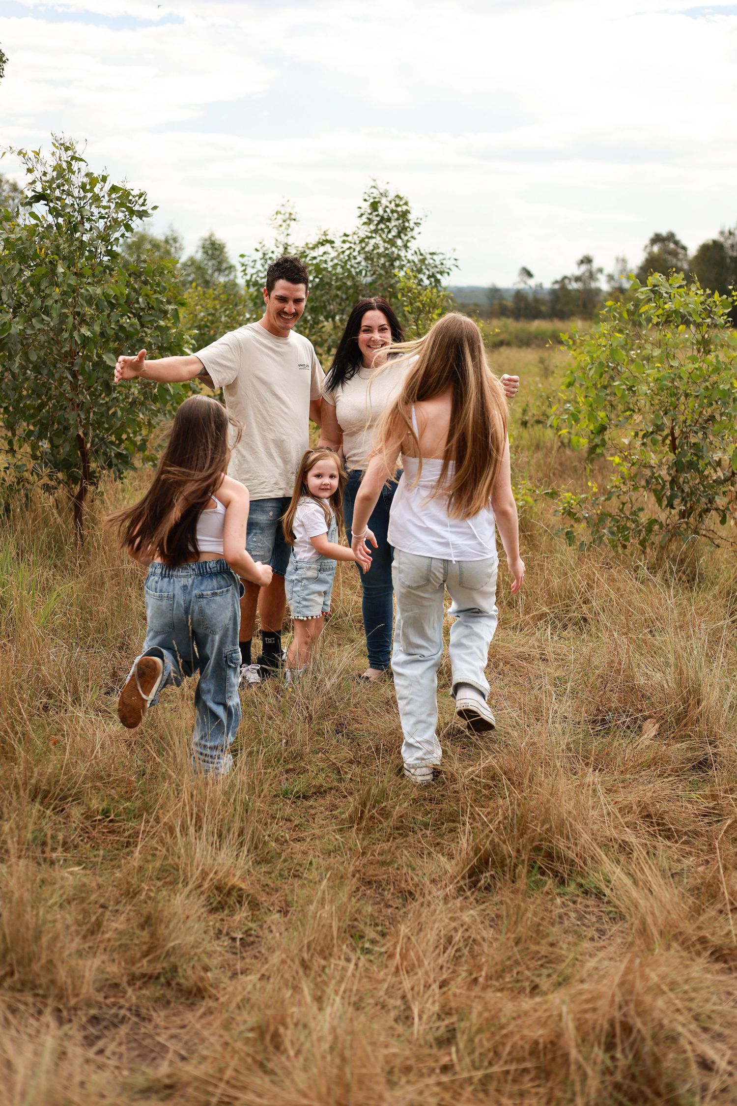 A family walking together through a sunlit meadow with tall grass and scattered trees in the background.