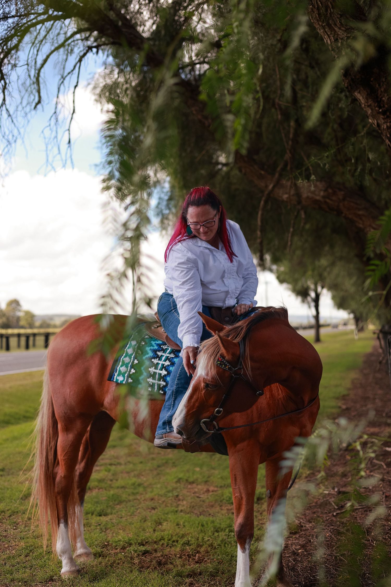 A rider mounted on a chestnut horse grazes along a grassy hillside on a sunny afternoon.
