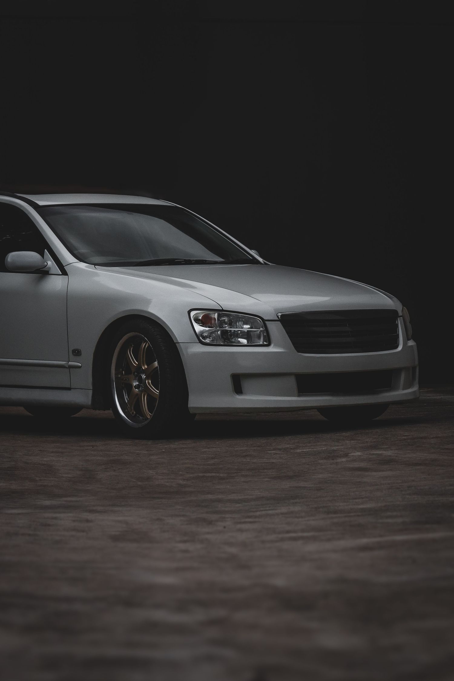 A lowered Nissan stagea with aftermarket wheels sits parked in a dark moody setting.