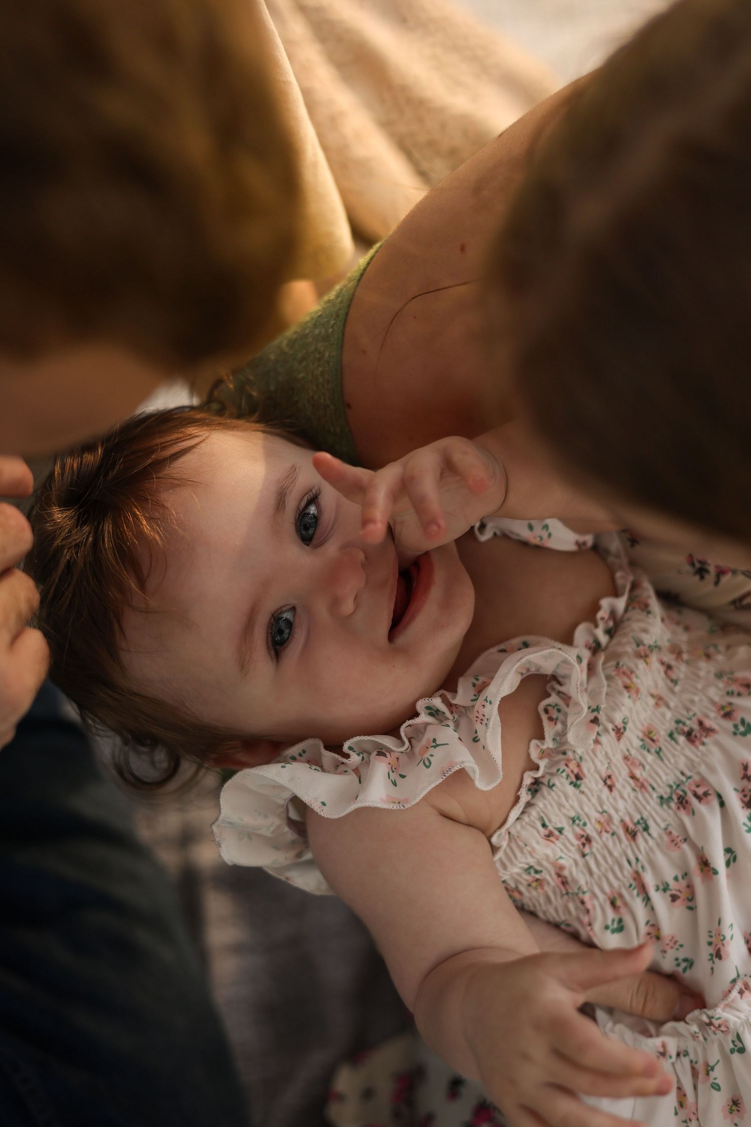 Smiling baby in floral outfit being held by mother in warm golden light.