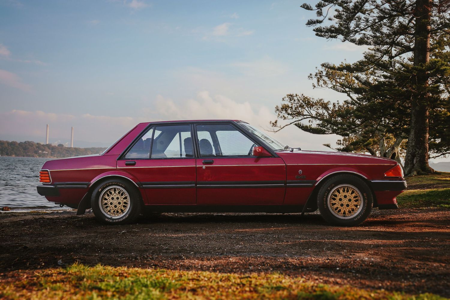 Classic red car parked on a coastal cliff overlooking the ocean during sunset.