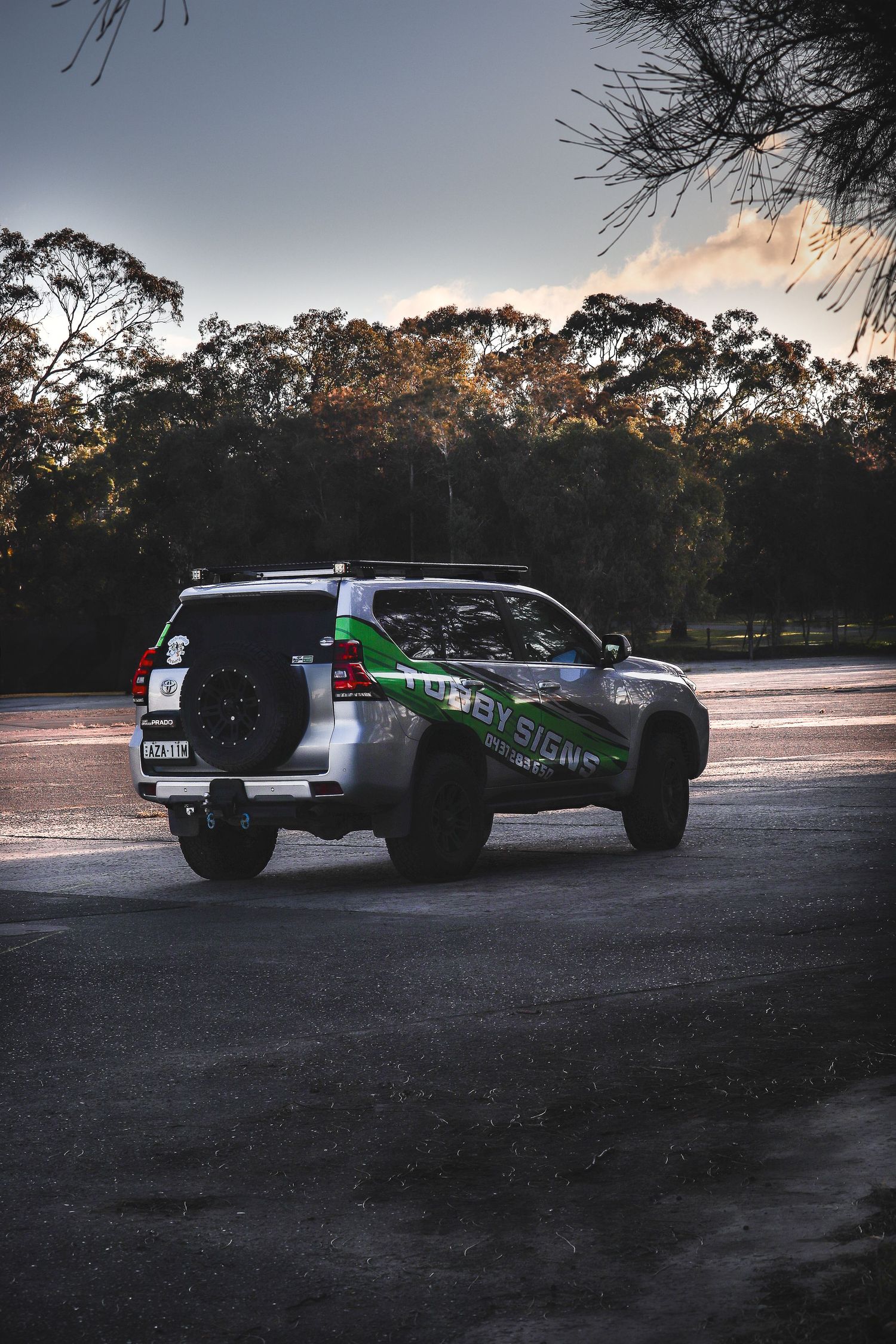 SUV parked on asphalt at dusk with forest silhouettes in background.