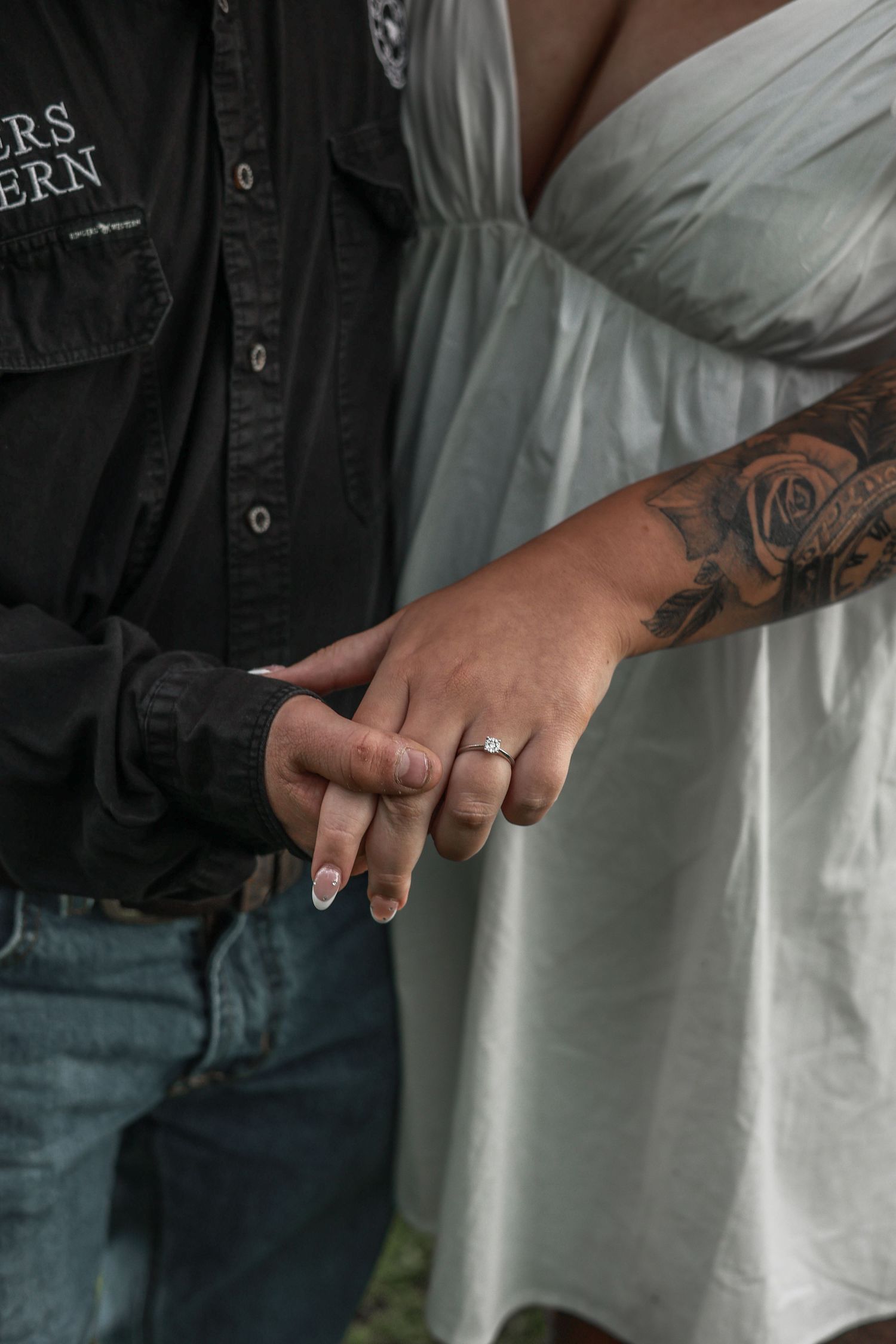 Close-up view of tattooed hands wearing rings against a backdrop of denim jeans and white shirt.