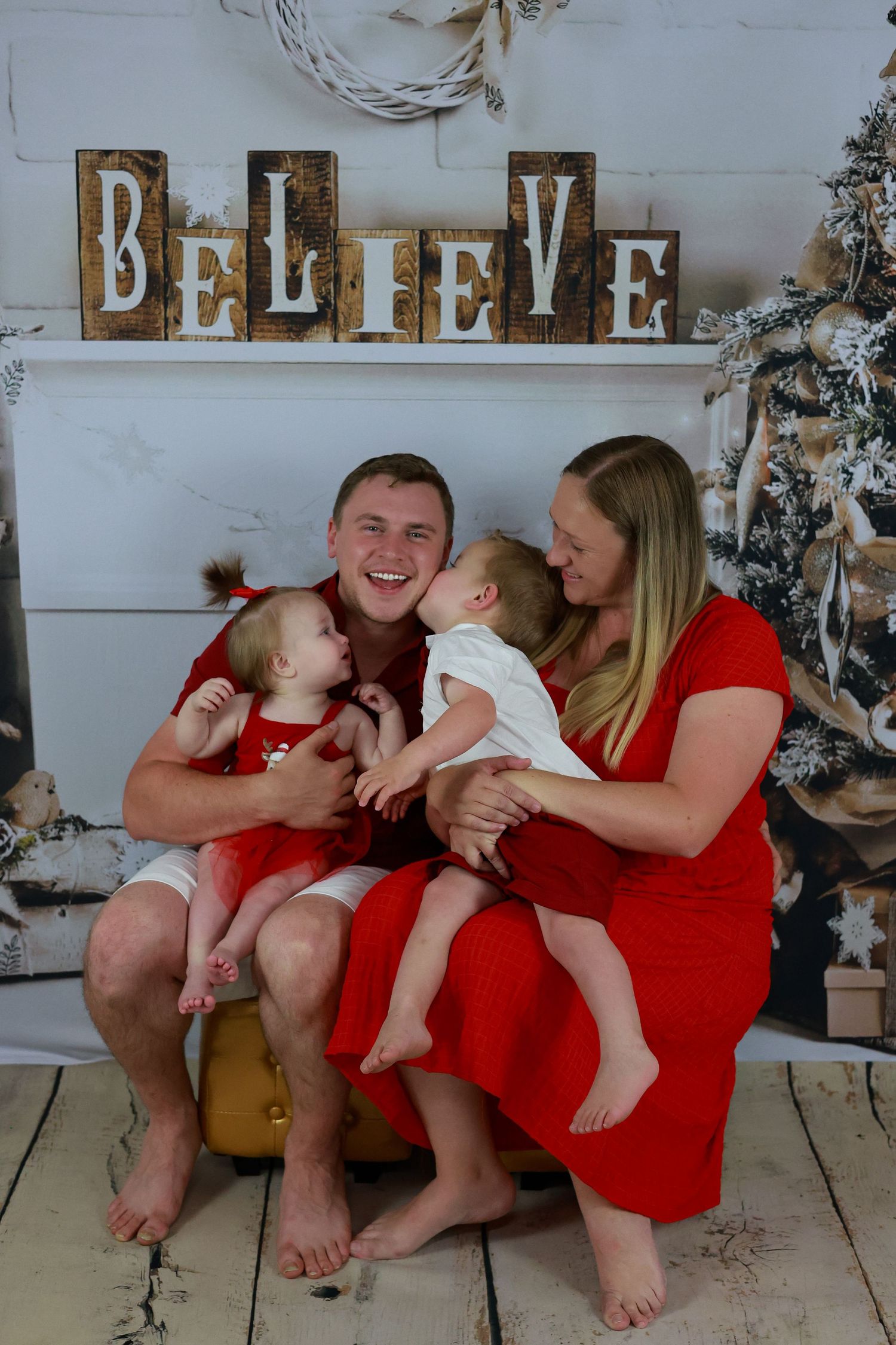A family wearing red outfits sits together in front of holiday decorations for a candid photo series.