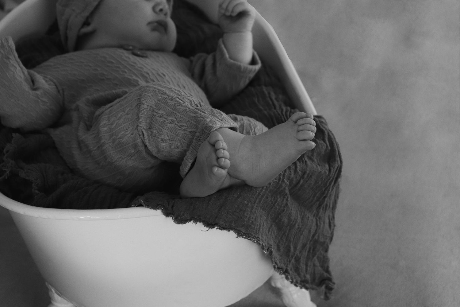 Black and white close-up photo of baby feet resting on a comfortable surface in natural light.