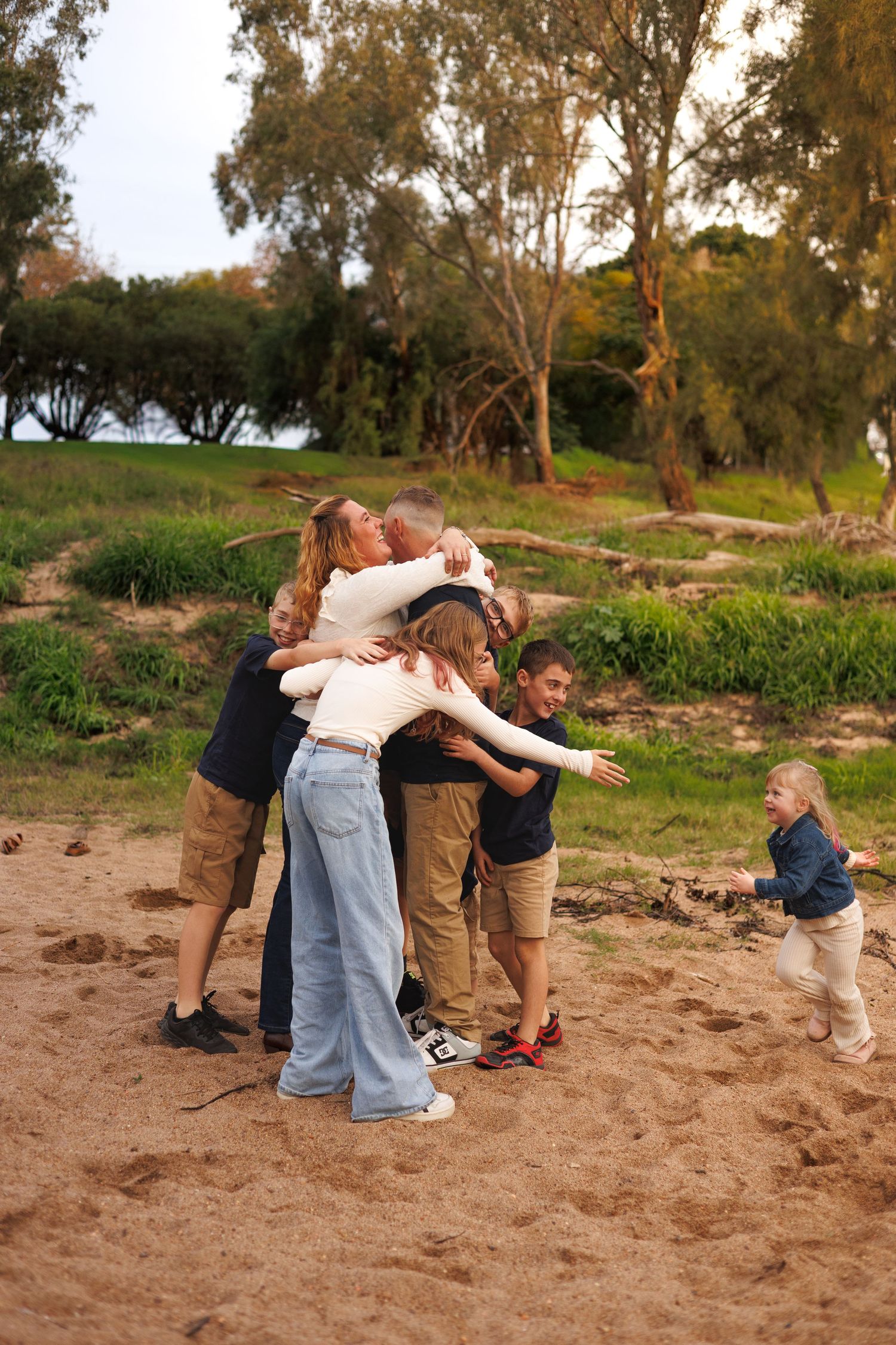 Happy family group hug on sandy beach surrounded by lush green trees outdoors.