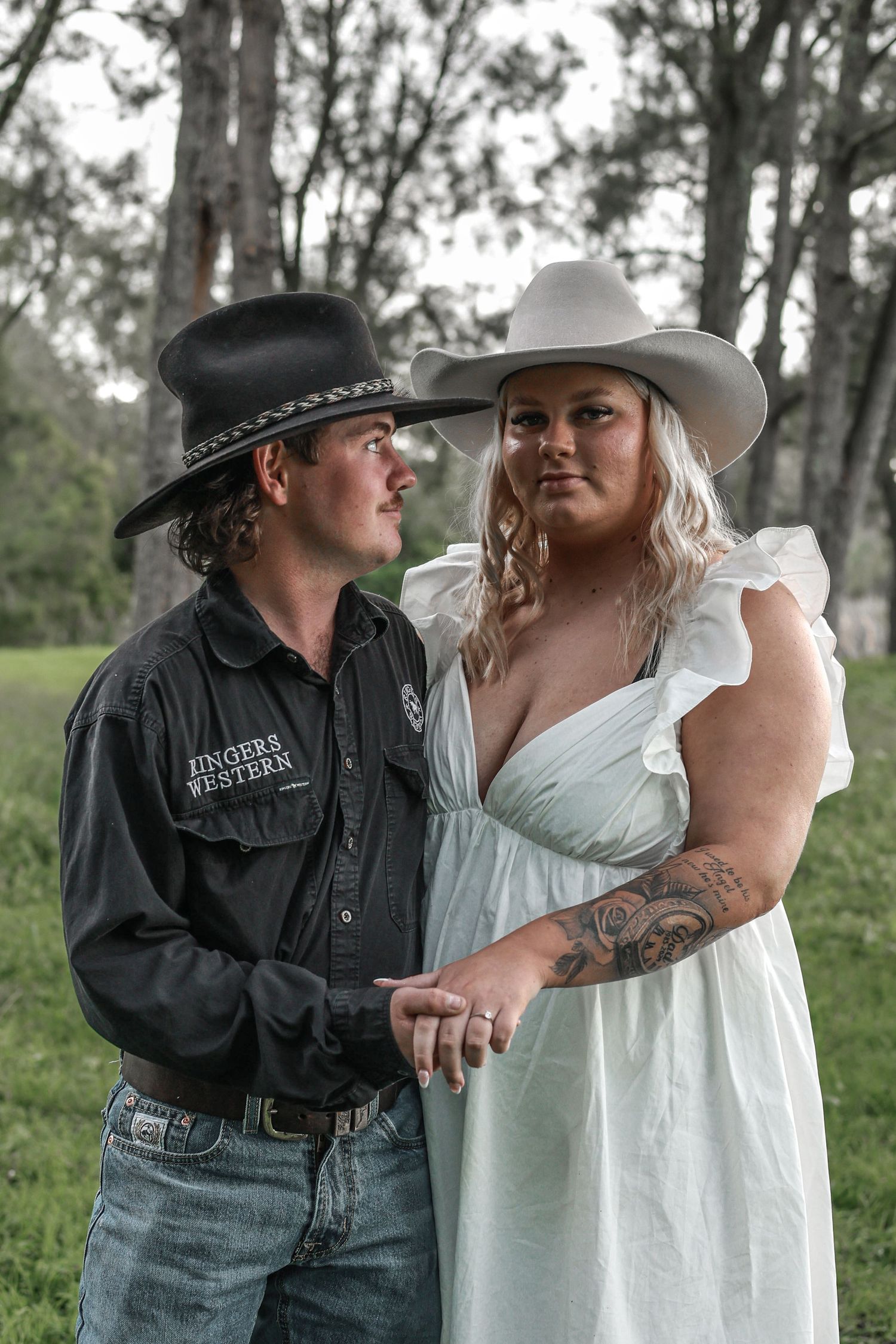 A couple in western attire share an intimate moment outdoors in a rustic setting.