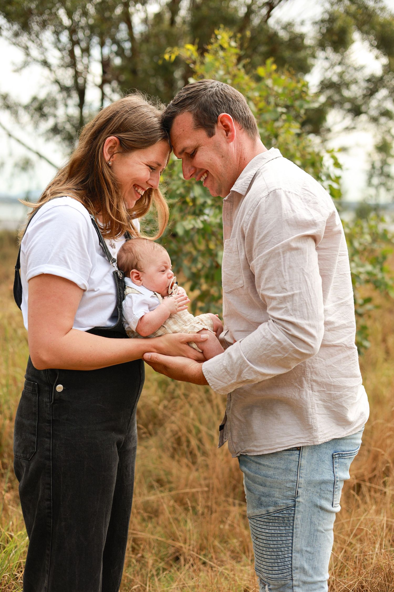 Happy couple smiling at their newborn baby outdoors in a natural bush setting.
