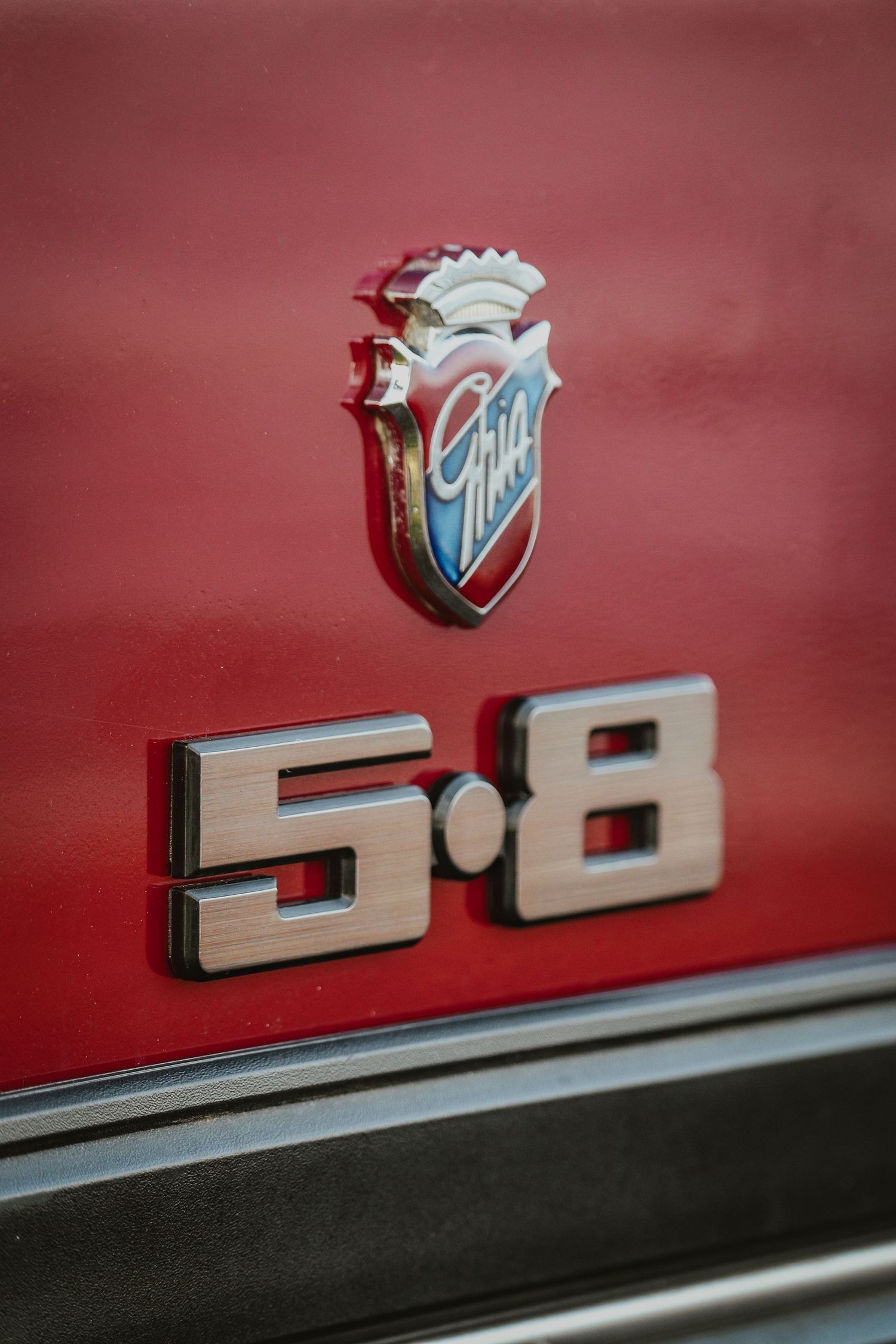 Chrome Ford 5.8 emblem and badge detail on red vintage car exterior showing classic automotive styling.