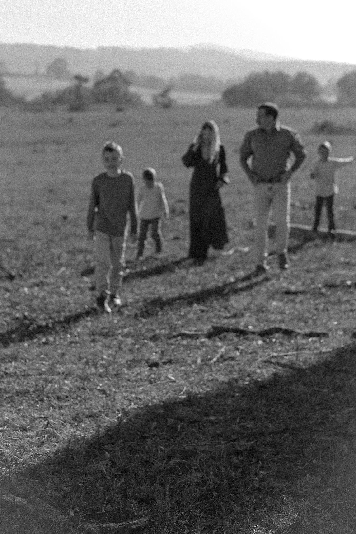 Black and white photo of a family walking together across an open rural field with rolling hills in the background.