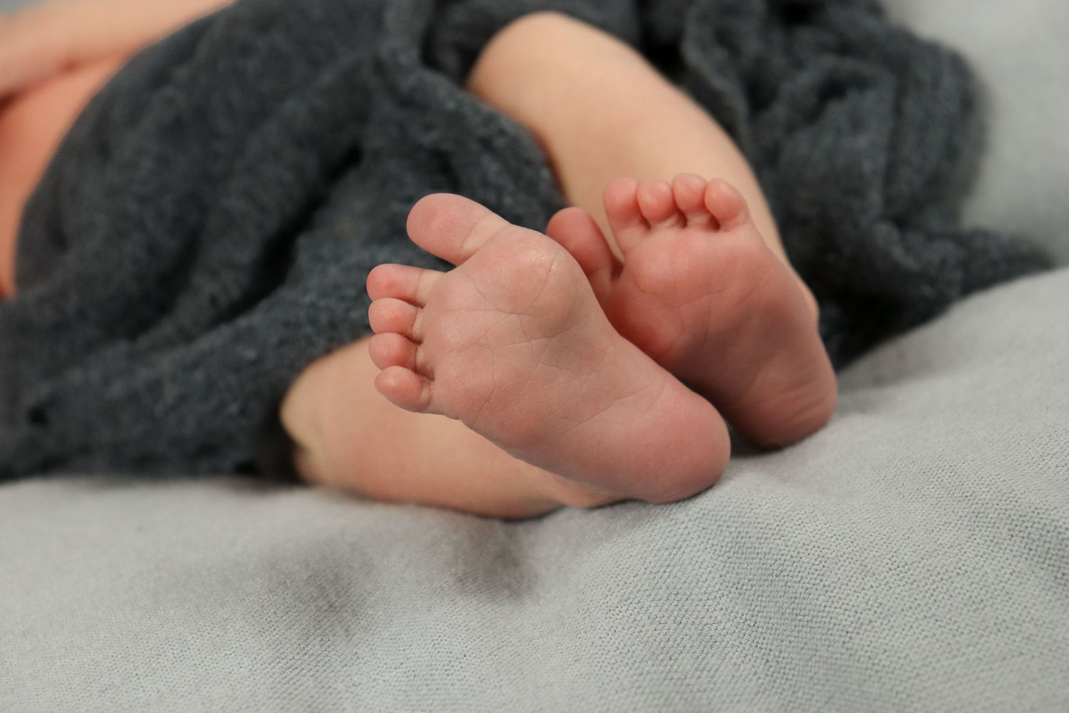 Tiny baby feet resting on soft gray fabric showing different angles and positions.