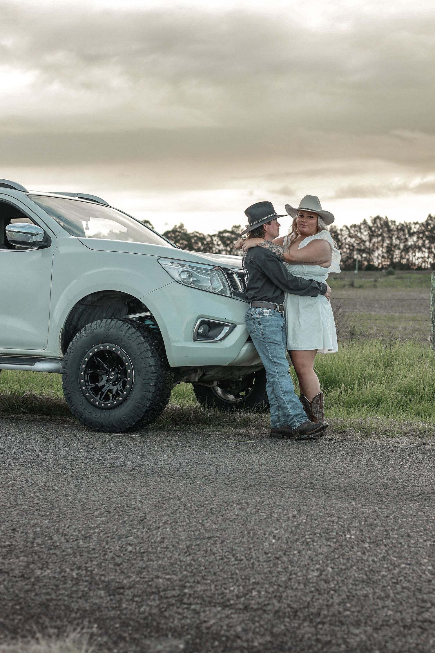 A white pickup truck parked on a gravel road with a couple beside it.