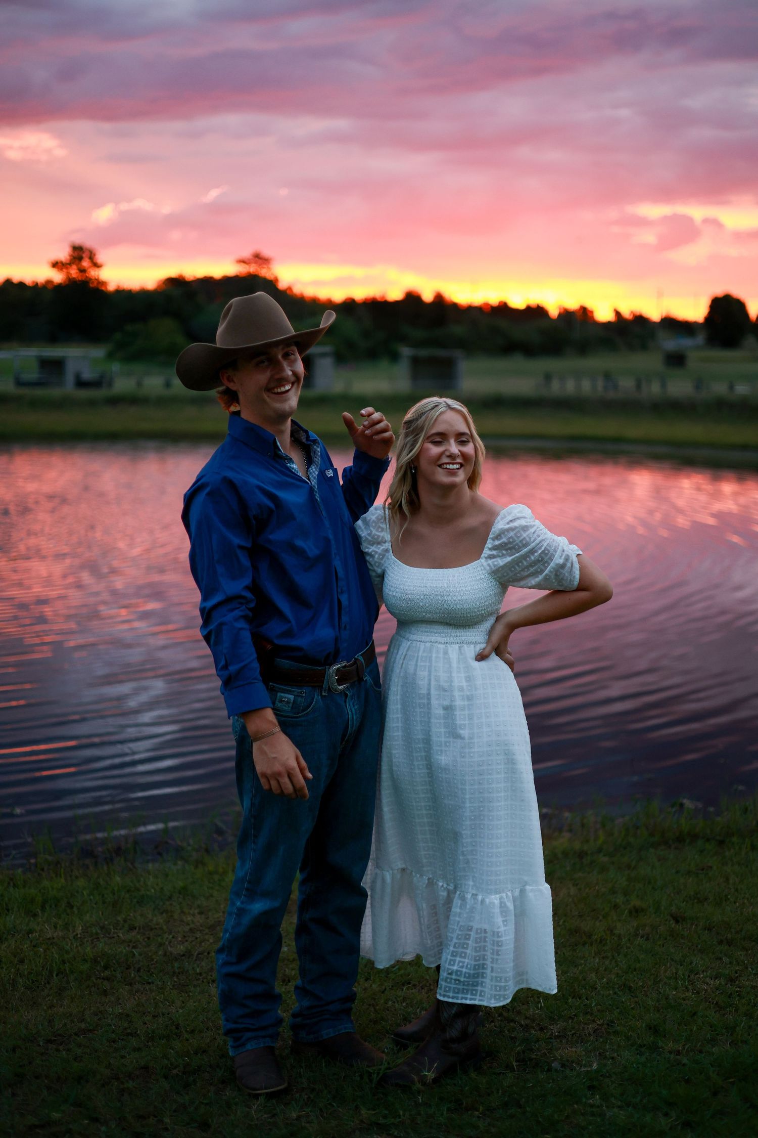 Sunset engagement photo session by a lake with a couple in casual attire enjoying tender moments at dusk.