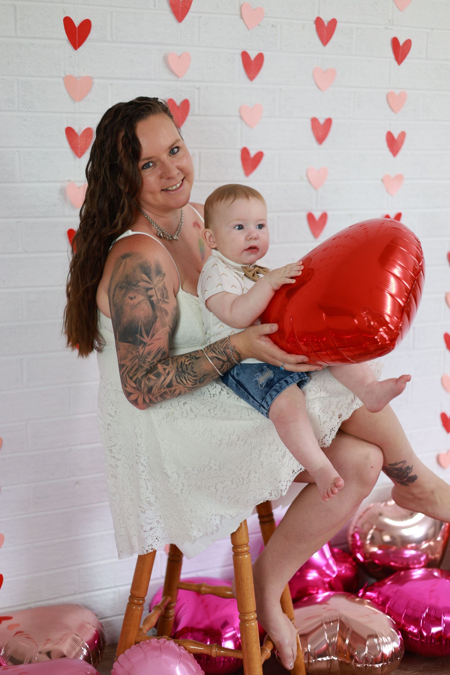 Pink and red valentine-themed photoshoot with heart decorations on white brick wall background.