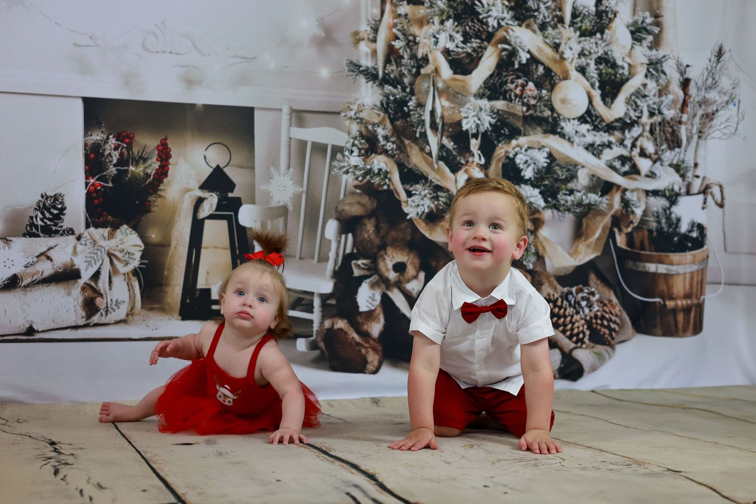 A baby in a red outfit crawls on the floor in front of a decorated Christmas tree with white ornaments.