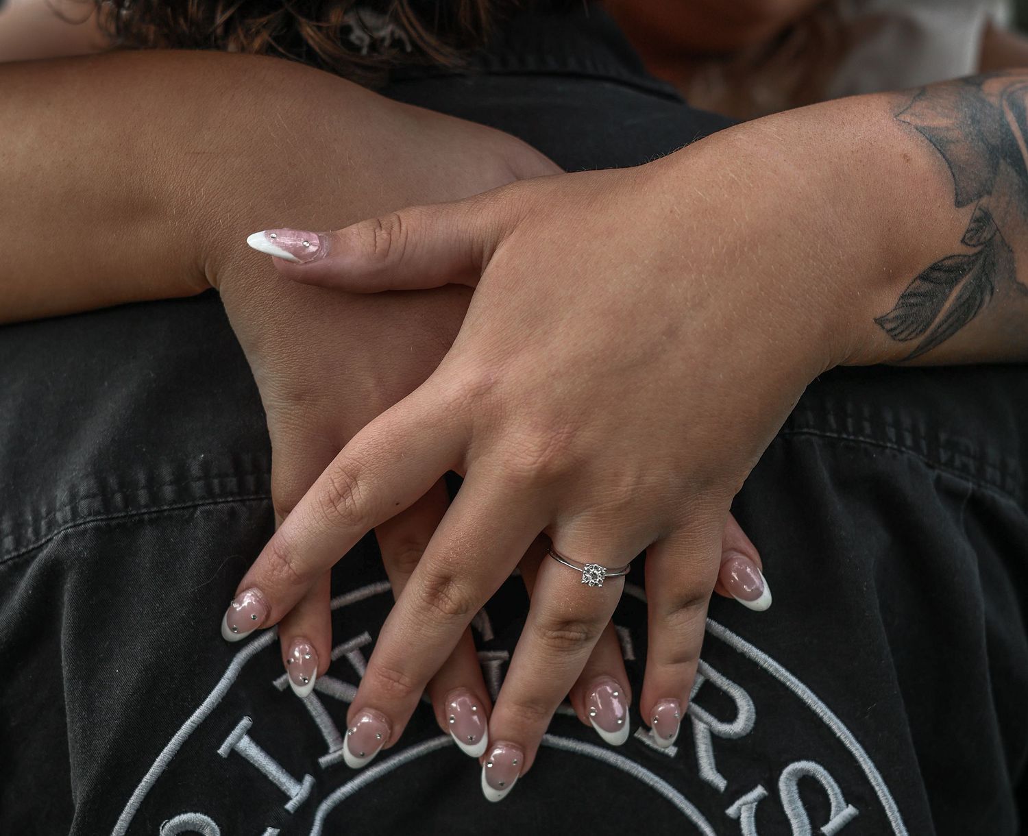 Close-up view of hands with white manicured nails resting on a black surface with white text.
