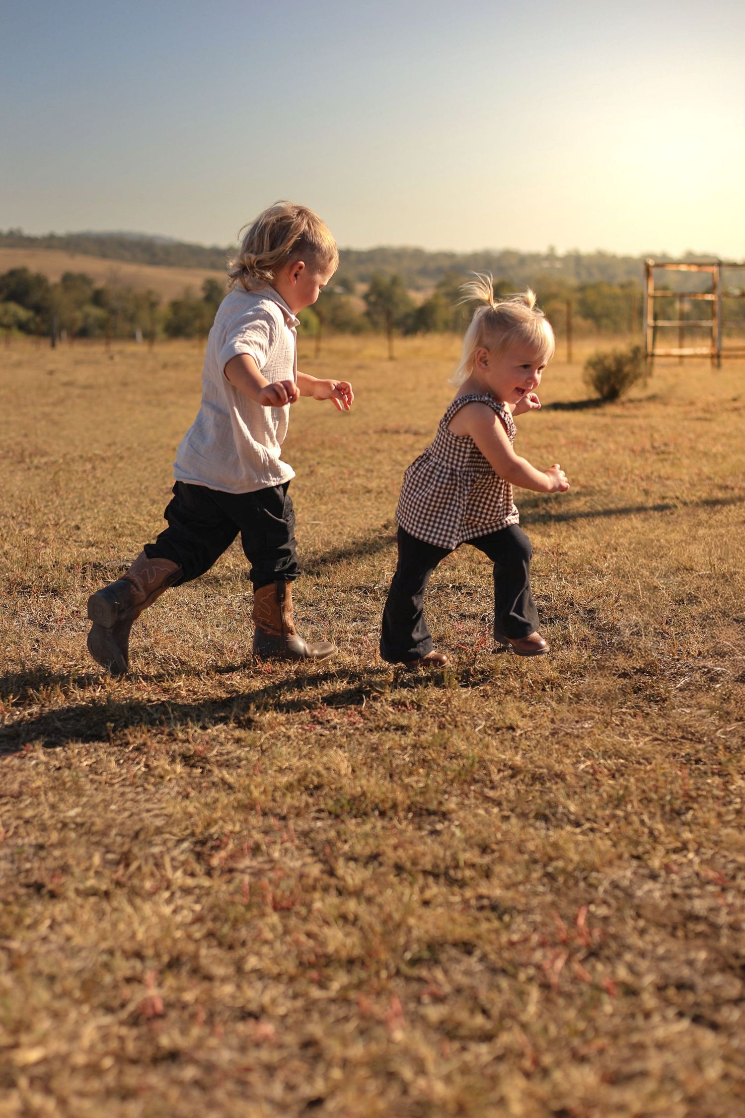 Two young children running and playing together in a sunny open field during golden hour.