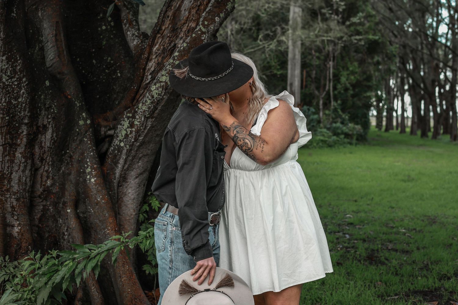 A couple in white attire embracing in a lush forest setting during a romantic photoshoot.