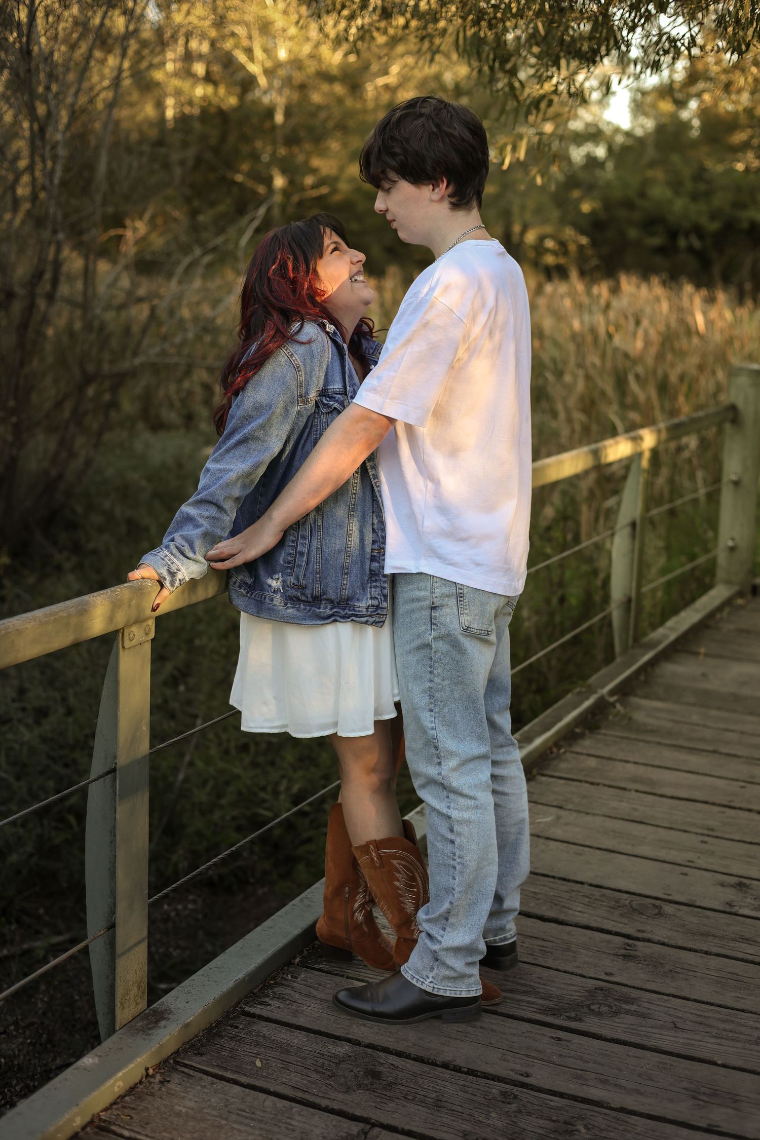 Young couple sharing a romantic moment on a wooden bridge surrounded by nature at golden hour.