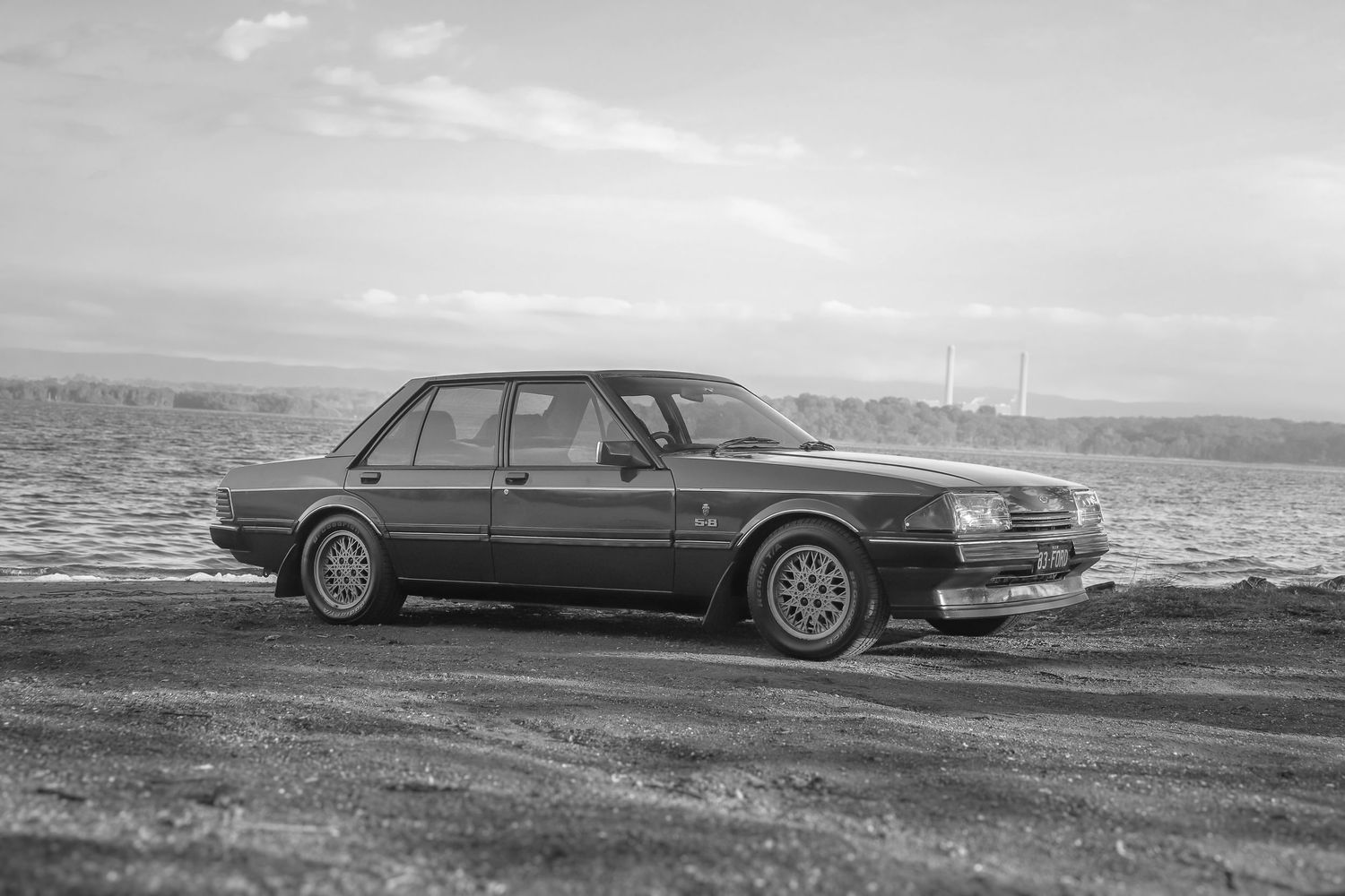 A vintage sedan parked on a coastal road with a dramatic ocean view in black and white photography.