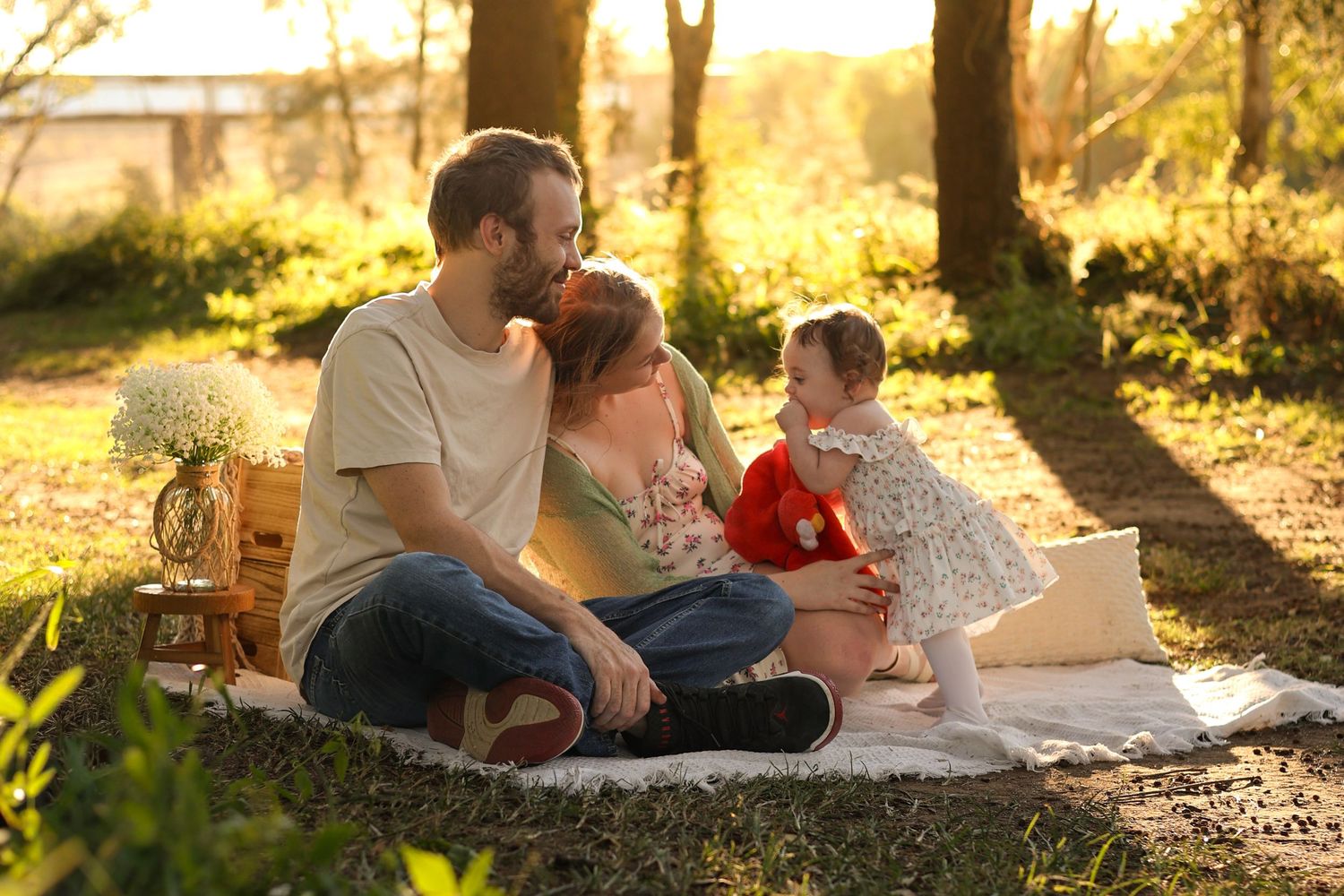 Family enjoying a golden hour picnic in the park, parents sitting on a blanket with their toddler outdoors.