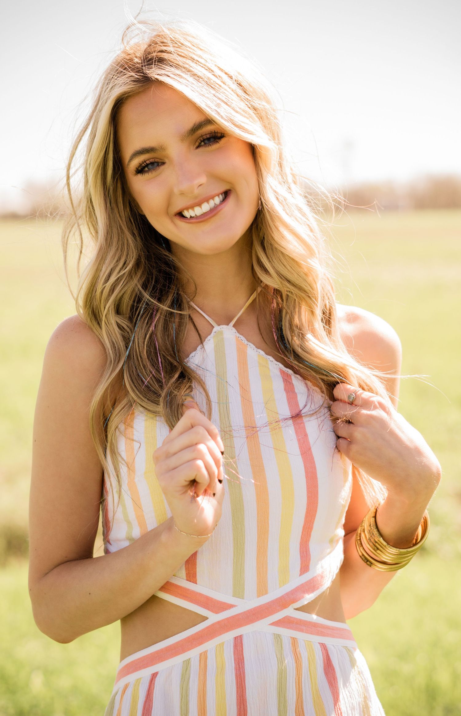 Warm outdoor portrait in pastel striped sundress with soft golden sunlight and natural meadow background.