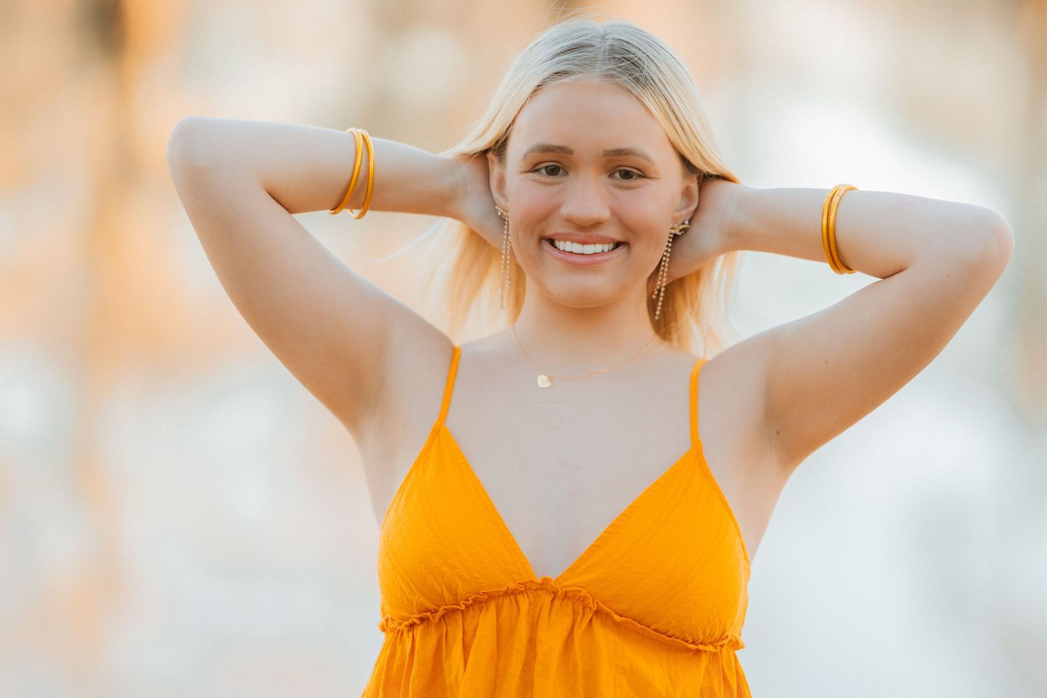 A person in a bright yellow sundress poses with hands behind their head during golden hour lighting.